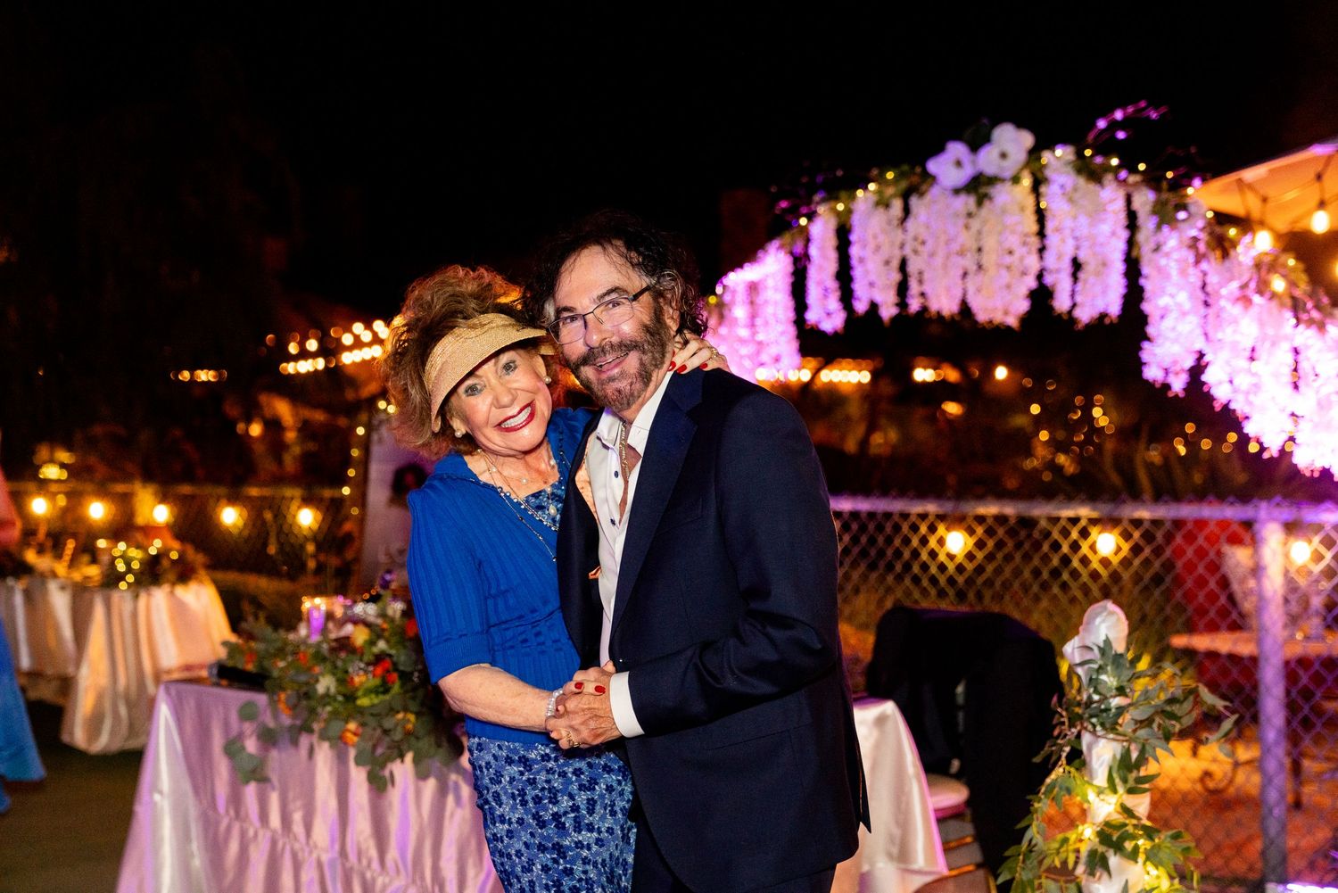 Evening wedding reception with purple floral decor and string lights creating a romantic ambiance.