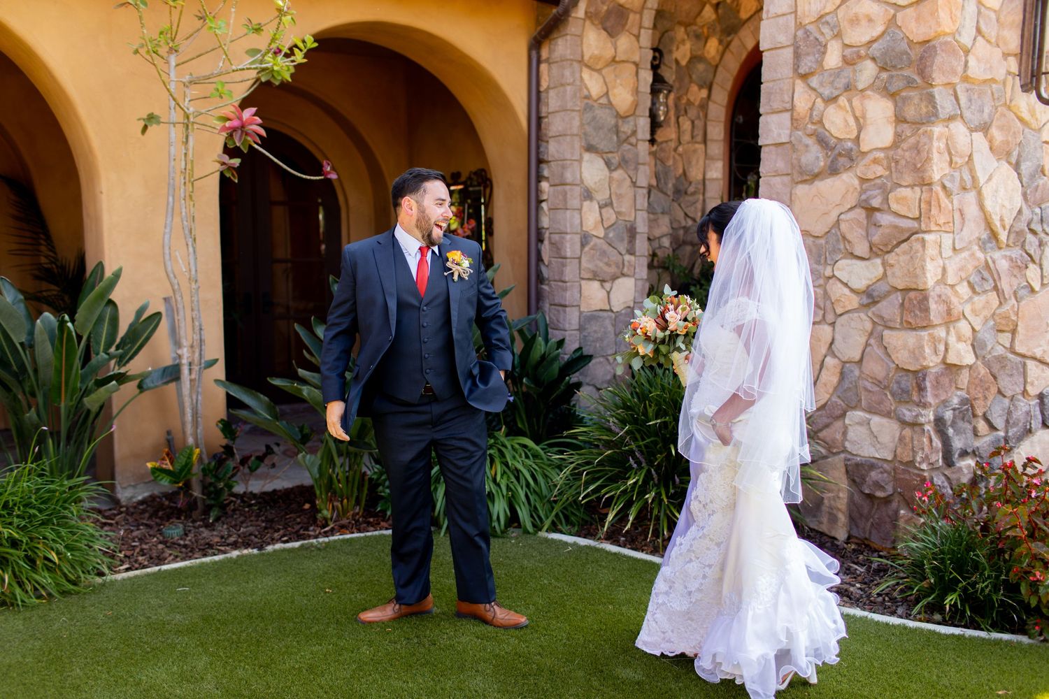 A romantic first look between newlyweds outside a rustic stone and stucco venue.