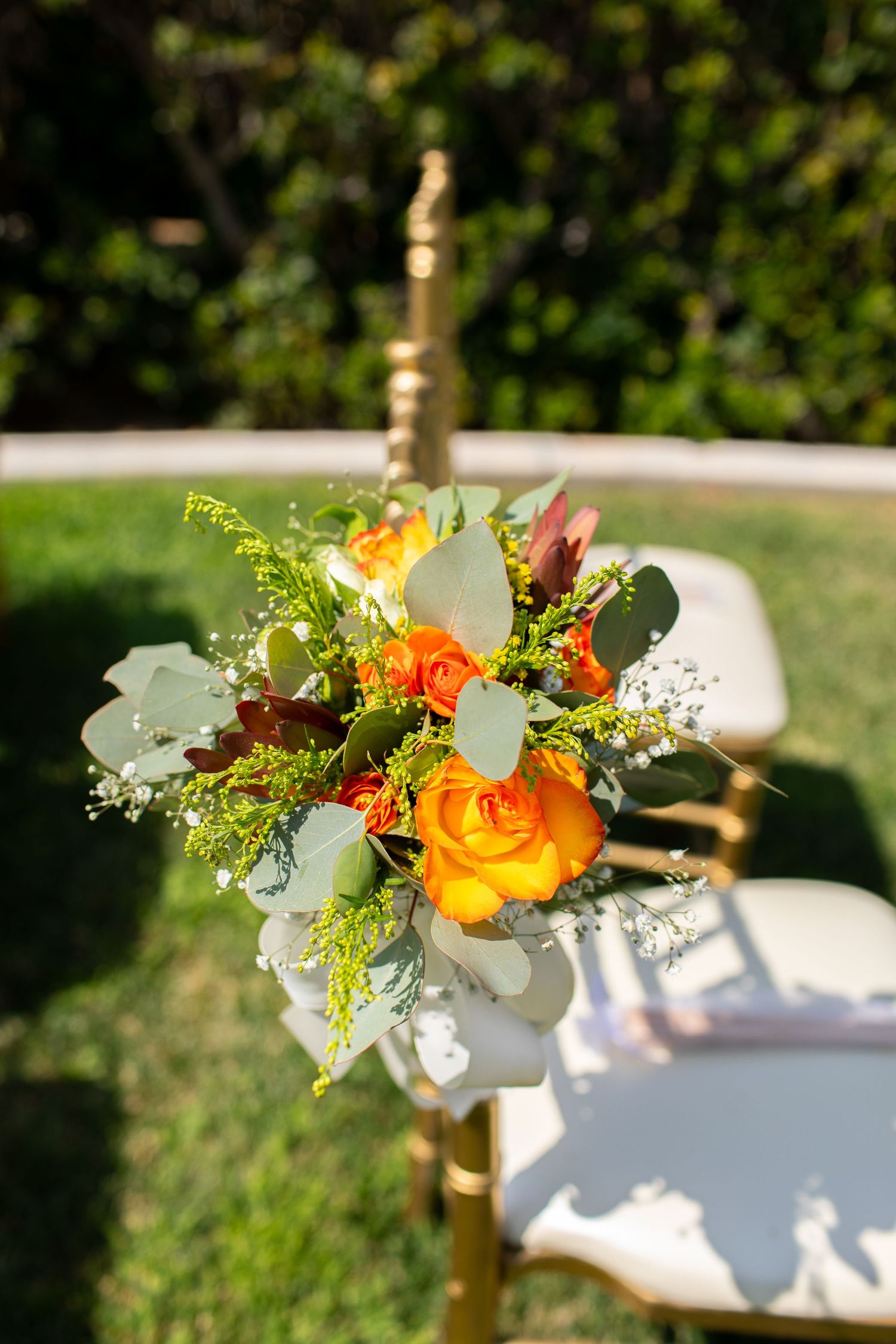 A vibrant floral arrangement with yellow roses and greenery adorns an outdoor chair at a sunny garden event.