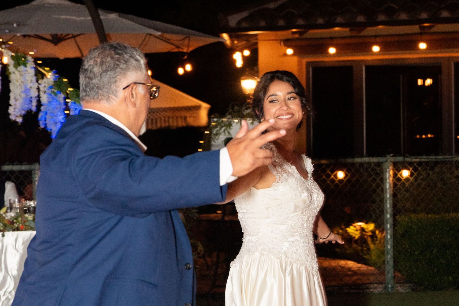 Couple shares a romantic dance moment under evening lights at outdoor reception.