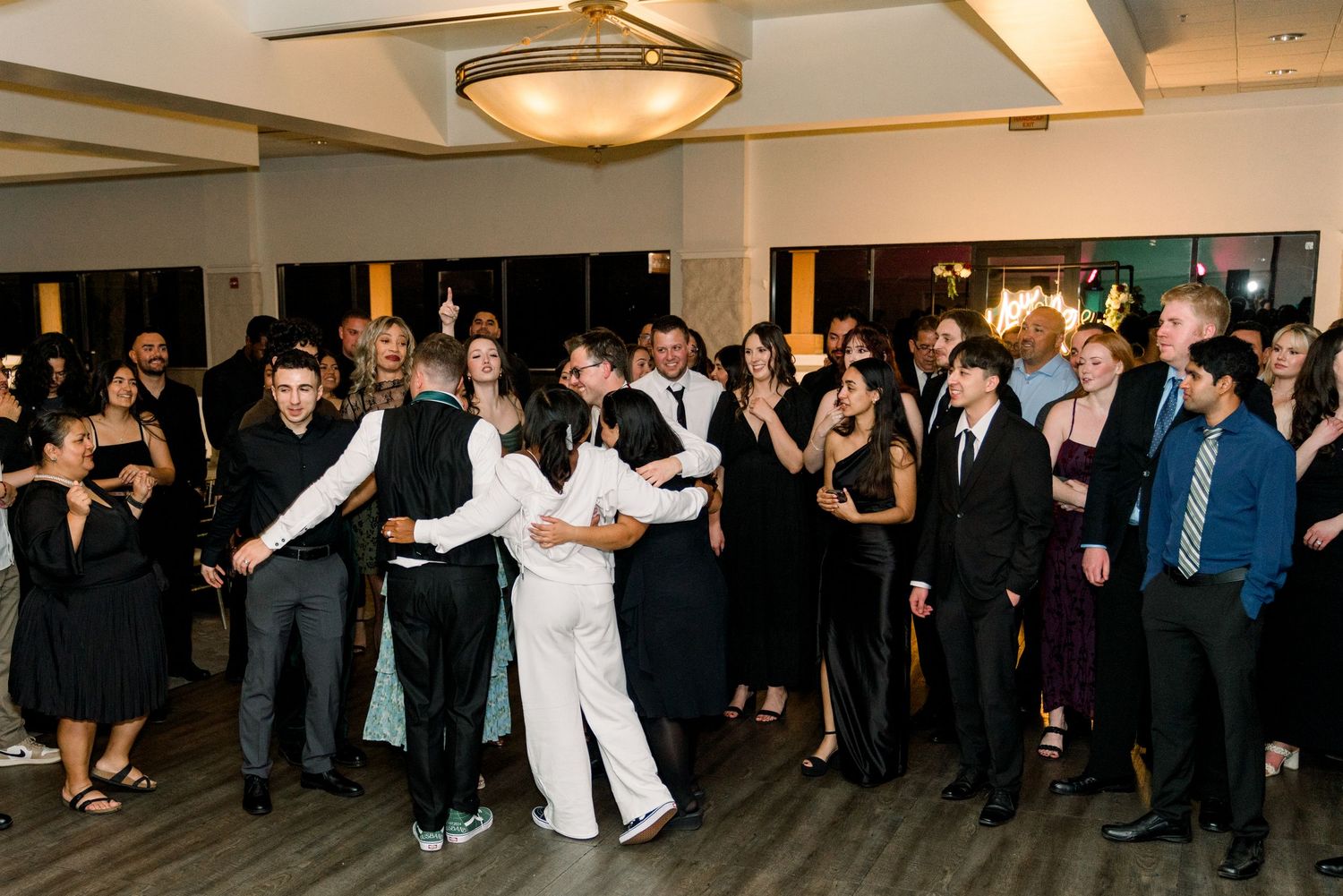 Wedding celebration with large group of guests dancing together in reception venue.