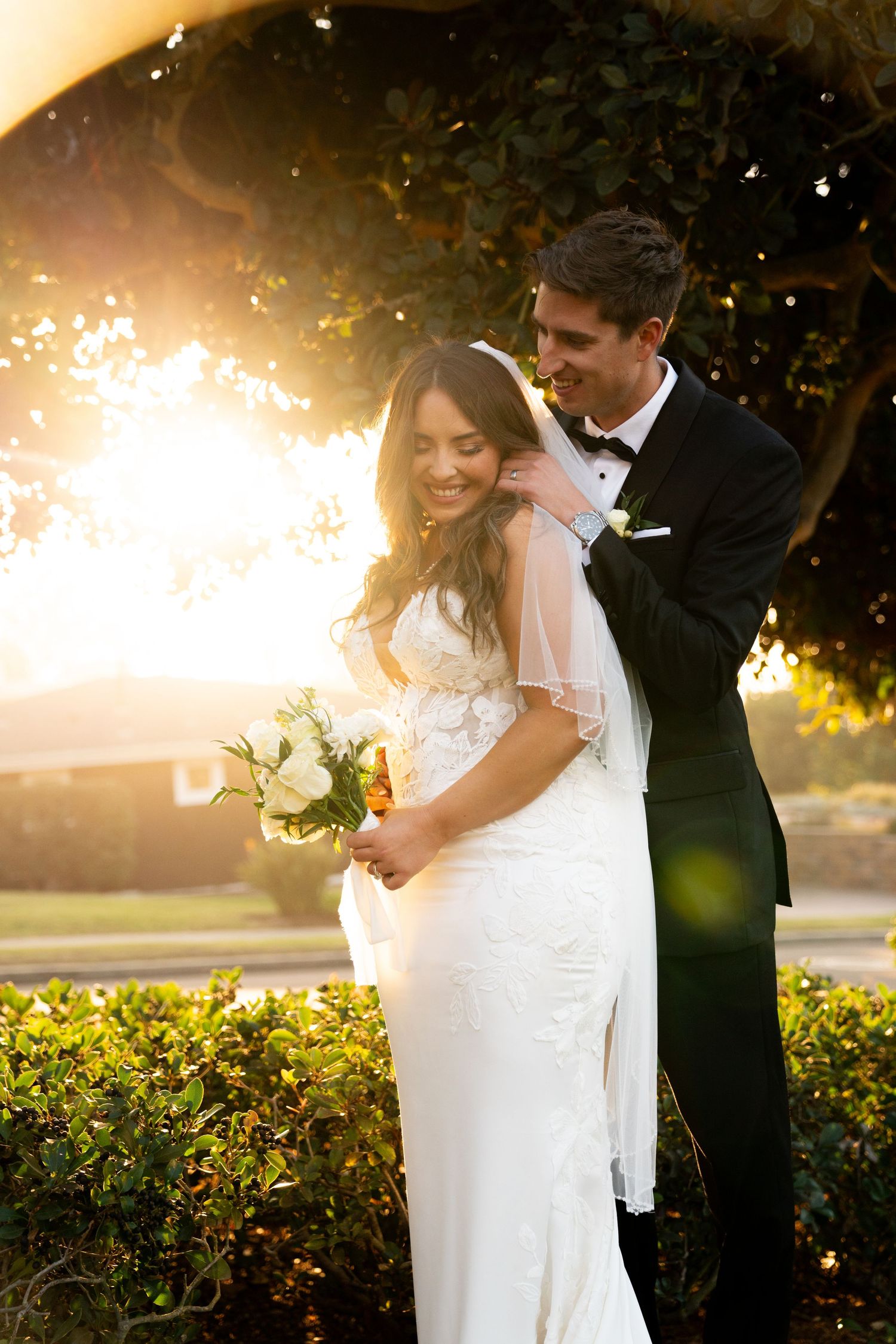 A couple shares an intimate moment at sunset with the bride holding a bouquet in her elegant white gown.