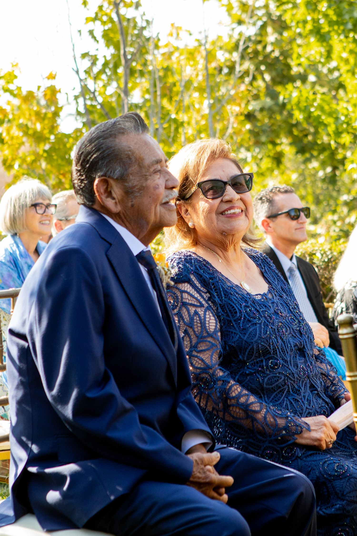 A couple in formal navy blue attire enjoying an outdoor celebration on a sunny day.
