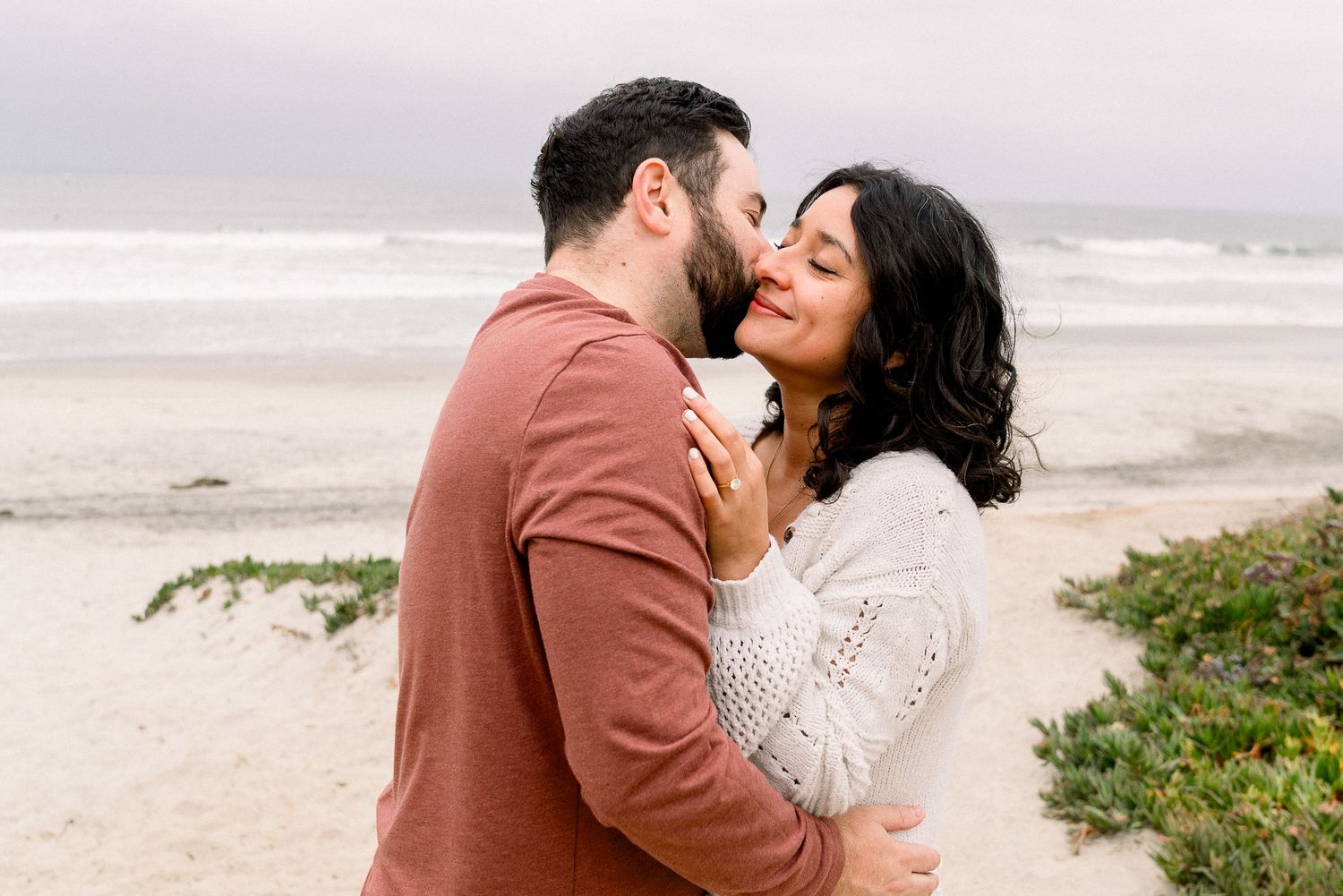 A romantic couple share an intimate moment together on a misty beach at sunset.