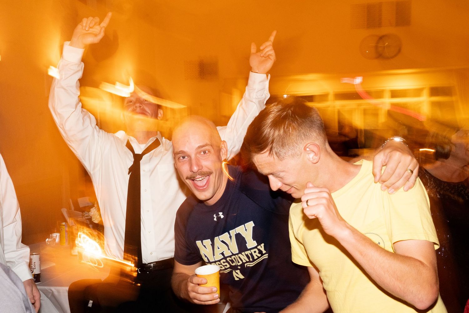 Wedding reception party guests celebrating energetically with drinks on the dance floor.
