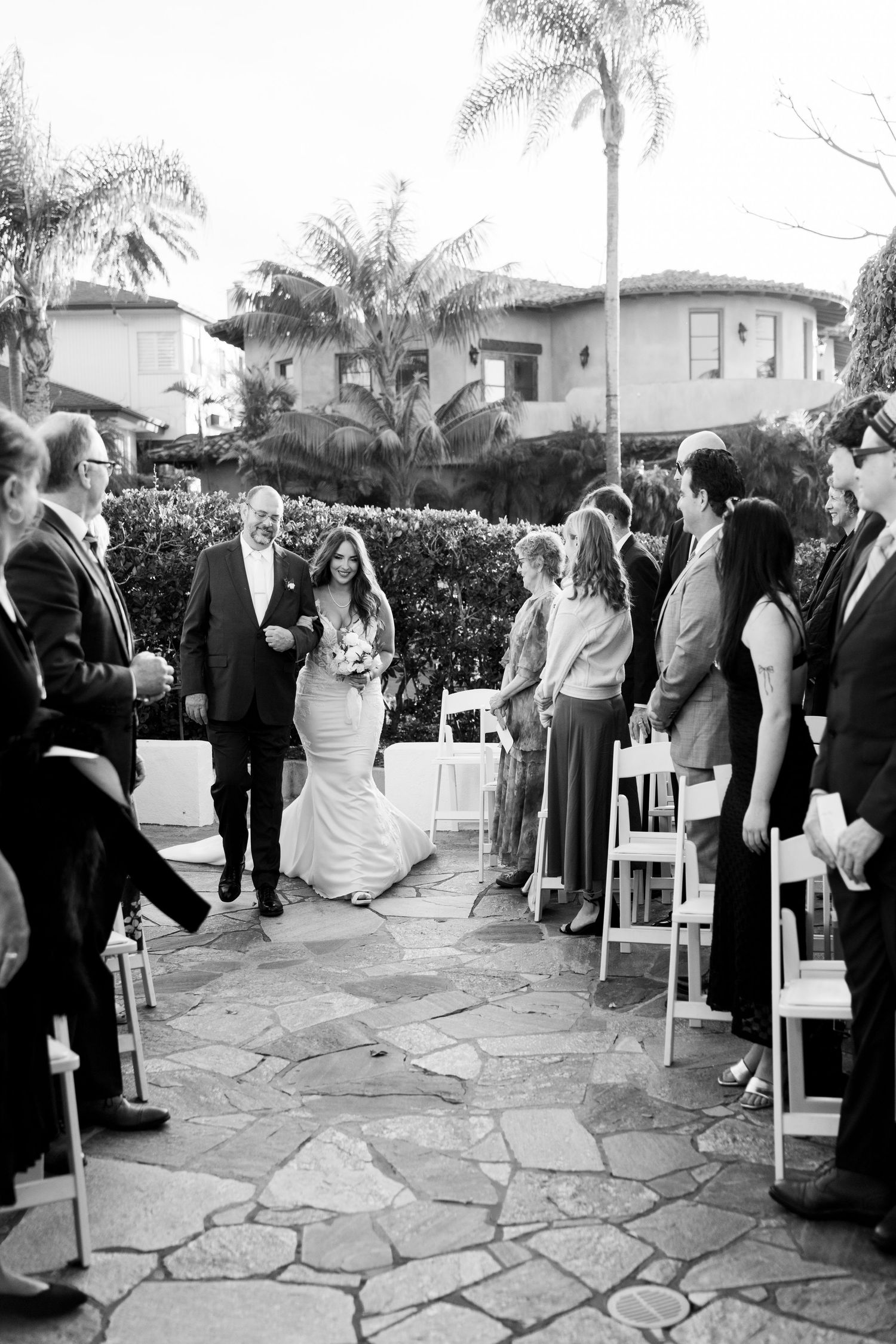 A black and white wedding ceremony on a stone patio surrounded by palm trees.