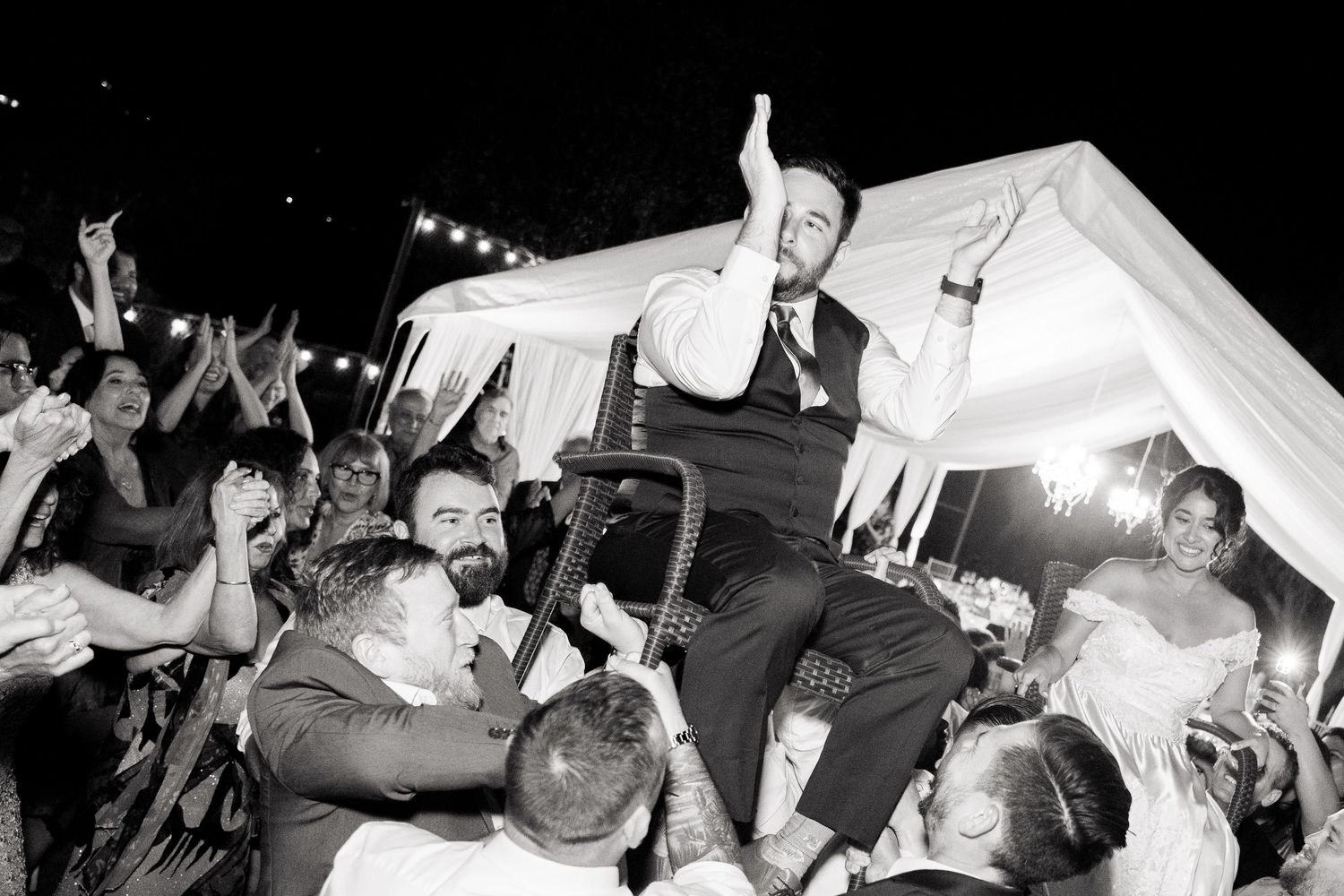 Black and white photo of wedding guests celebrating with crowd surfing during a lively reception party.