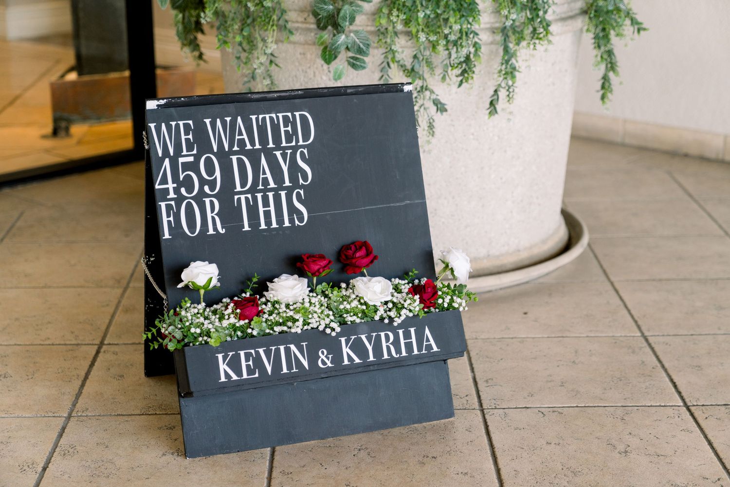 Wedding sign reading 'We waited 459 days for this' decorated with red roses.