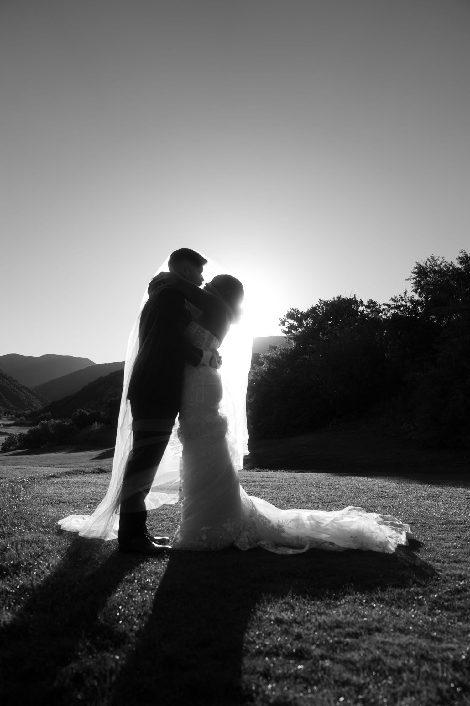 Silhouetted couple embracing on a hilltop at sunset creating a romantic black and white portrait.