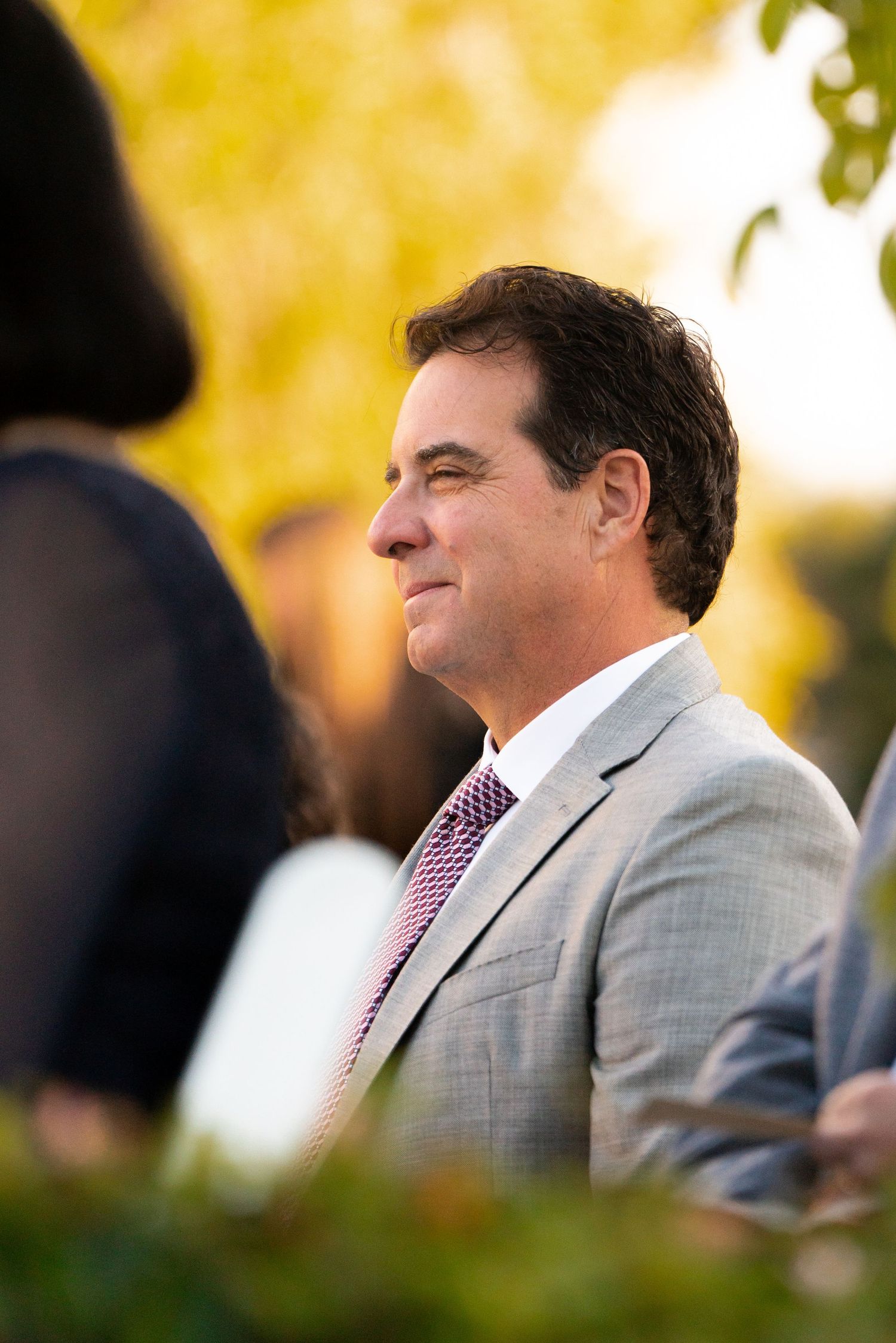 A wedding guest in a light grey suit and pink tie watches the ceremony.