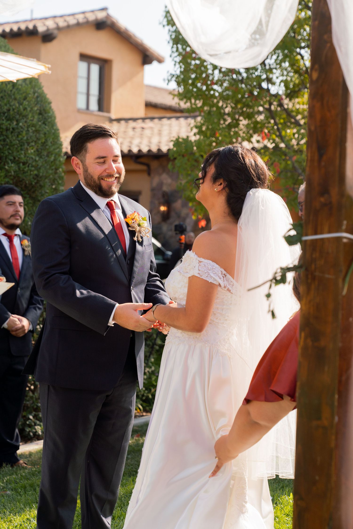 A joyful wedding ceremony takes place in front of a rustic Mediterranean villa with landscaped gardens.