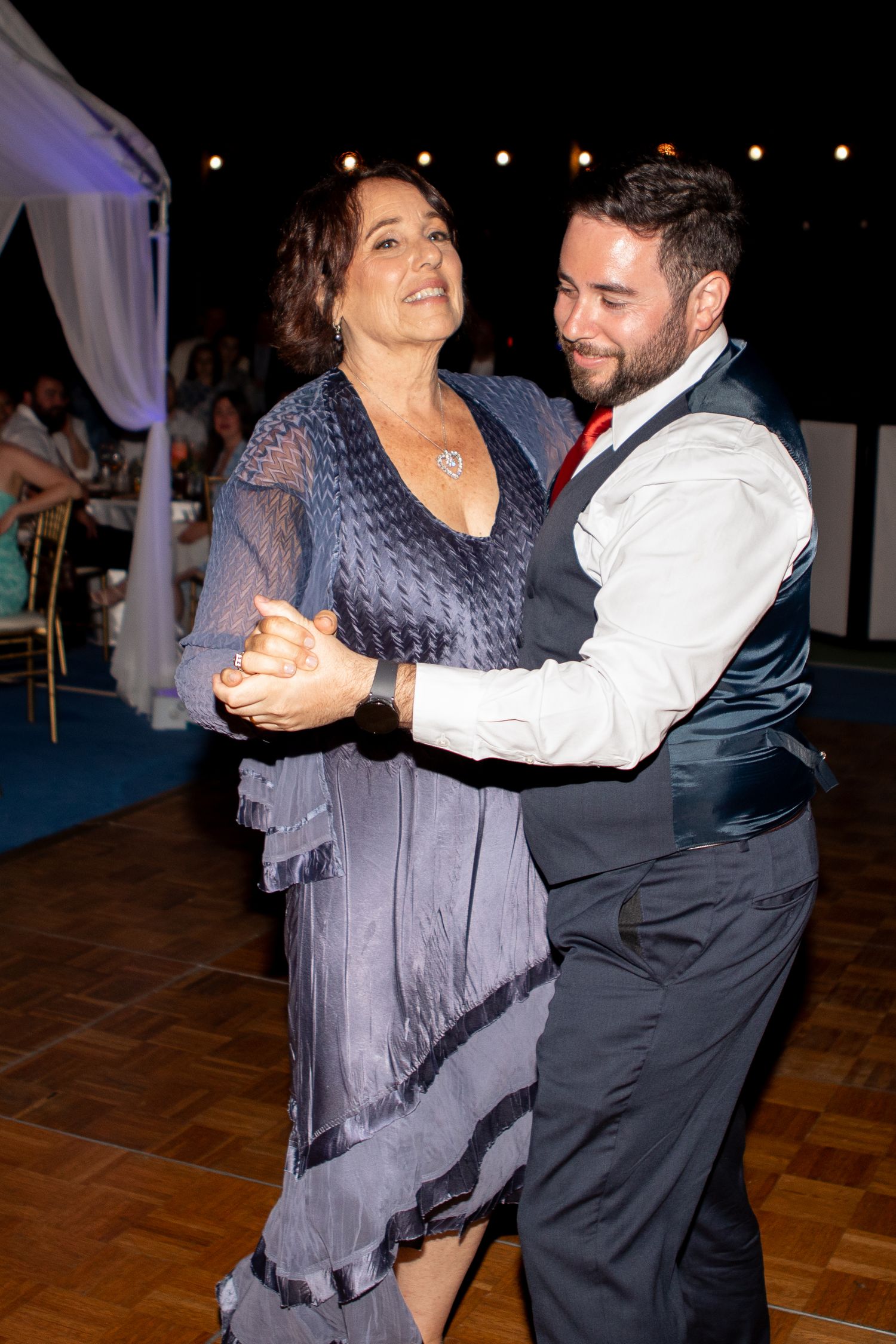 Elegant couple dances together at evening reception with string lights in background.