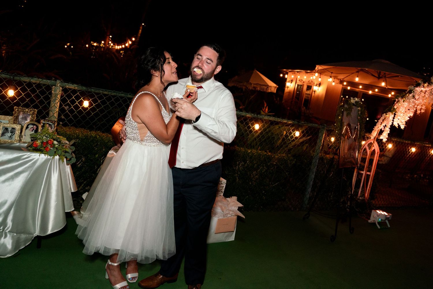 A couple shares a playful dance moment at their outdoor evening wedding reception with string lights.