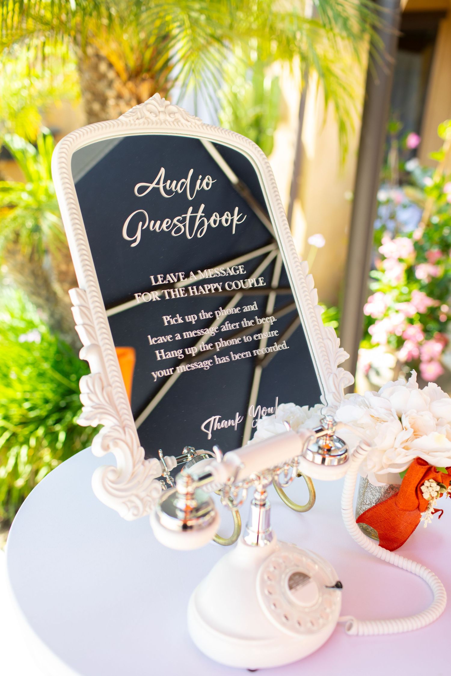 An elegant framed audio guestbook sign at a wedding with decorative details in a garden setting.