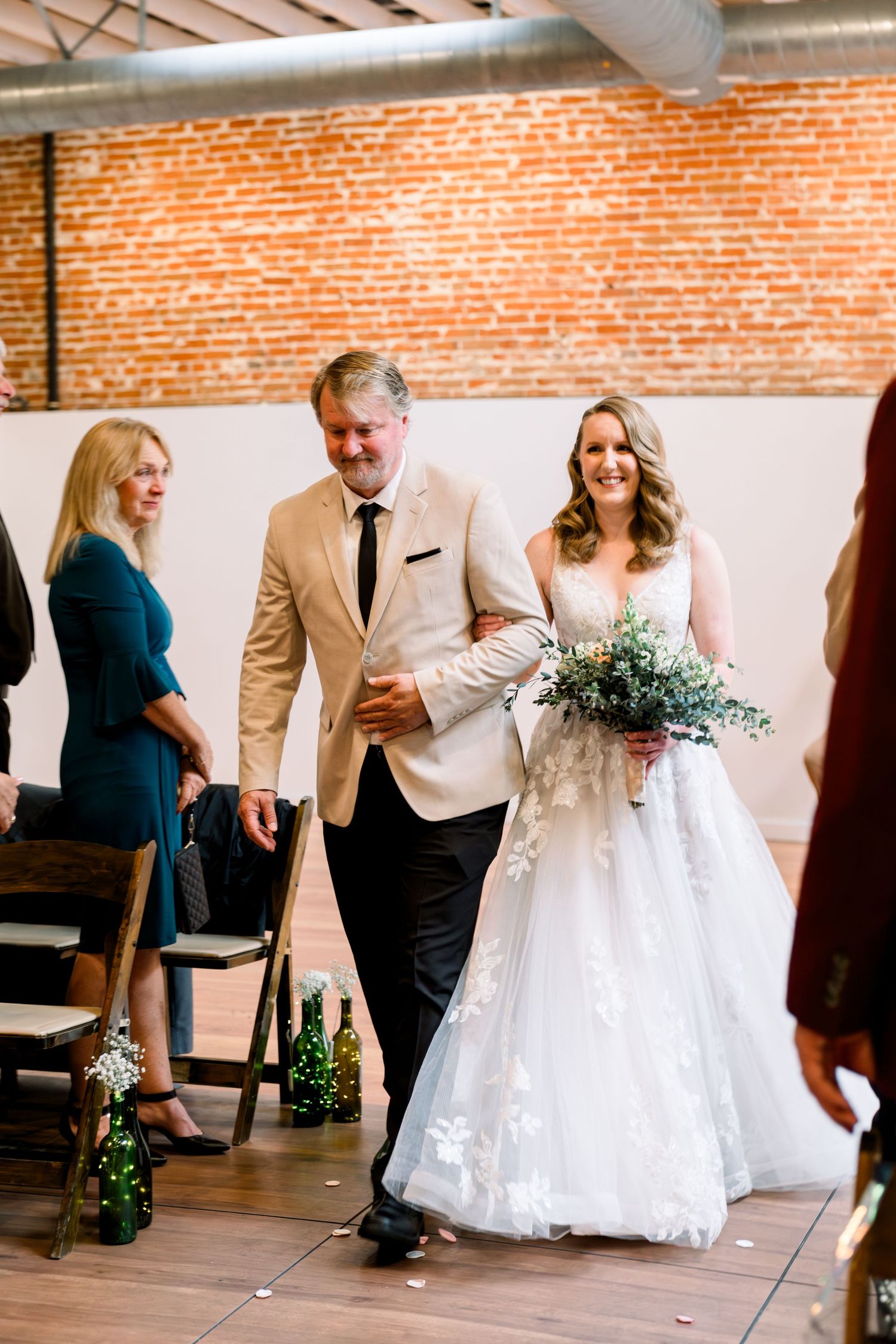 Beautiful indoor ceremony in industrial brick venue with light wood floors and elegant white wedding bouquet.