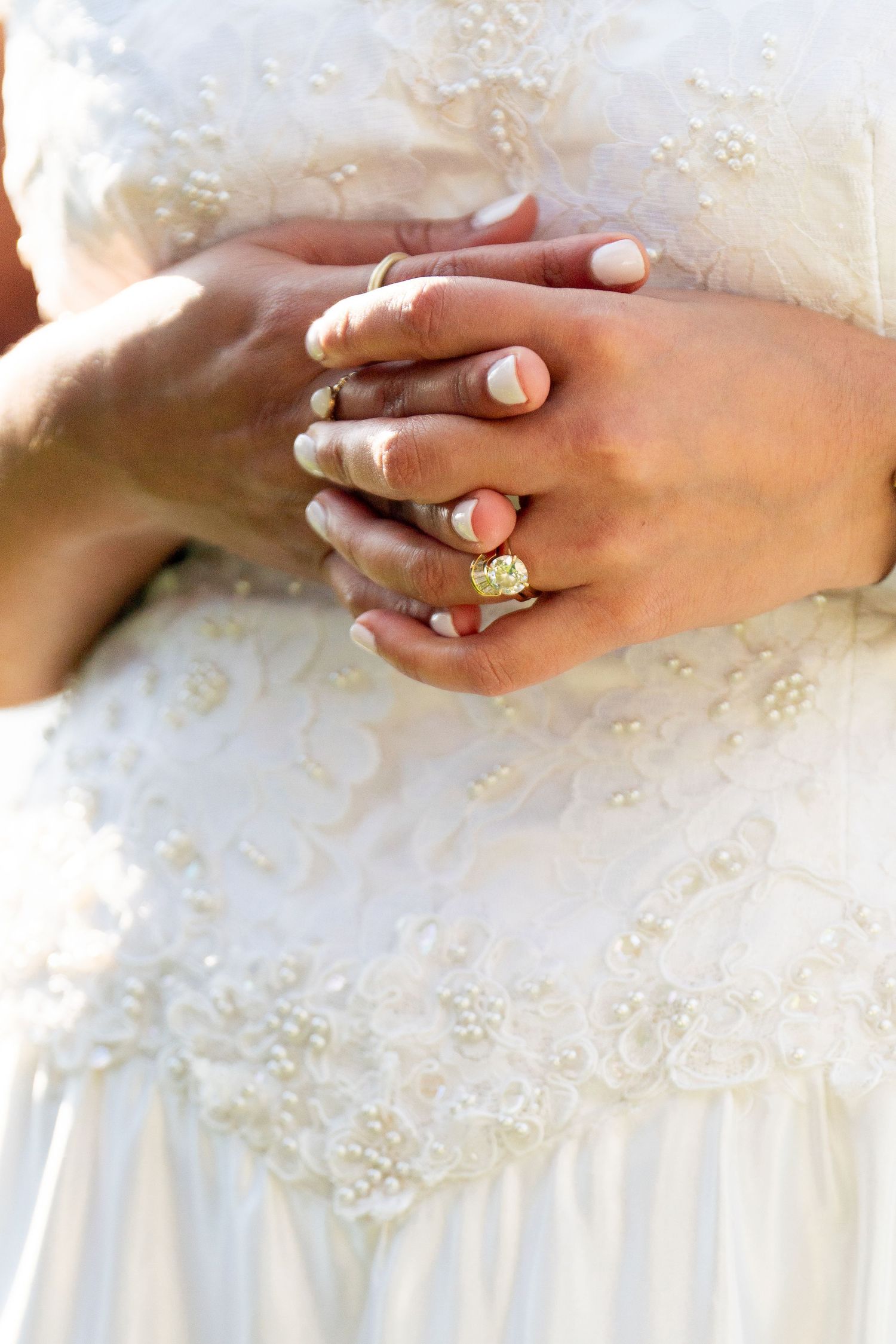 Close-up of hands wearing wedding rings against a white lace dress.