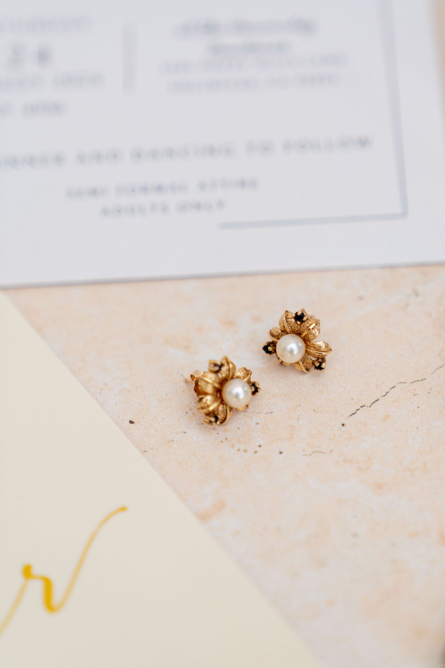 Close-up of delicate gold pearl earrings against wedding stationery.