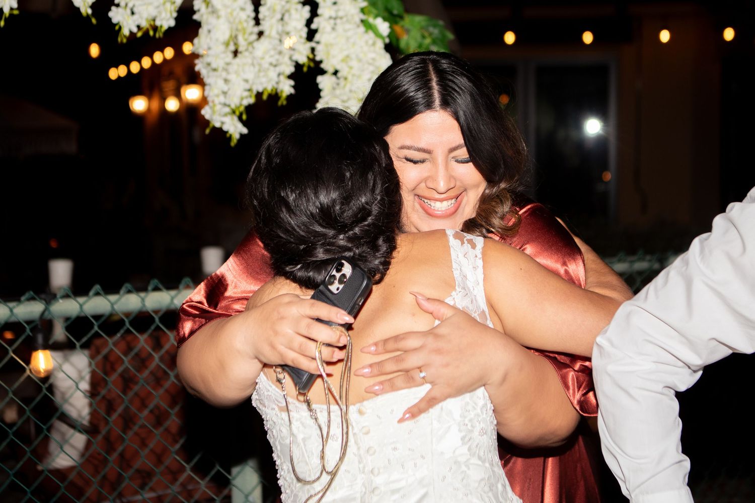 Emotional embrace shared during wedding reception celebrations under evening string lights.