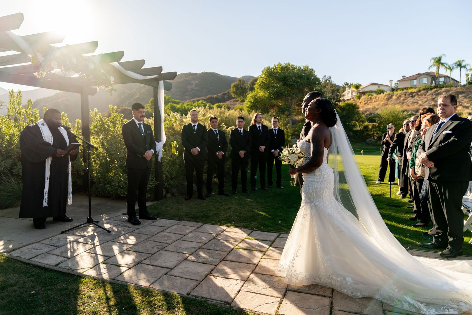 Wedding ceremony under pergola with mountain views as couple exchanges vows before guests.