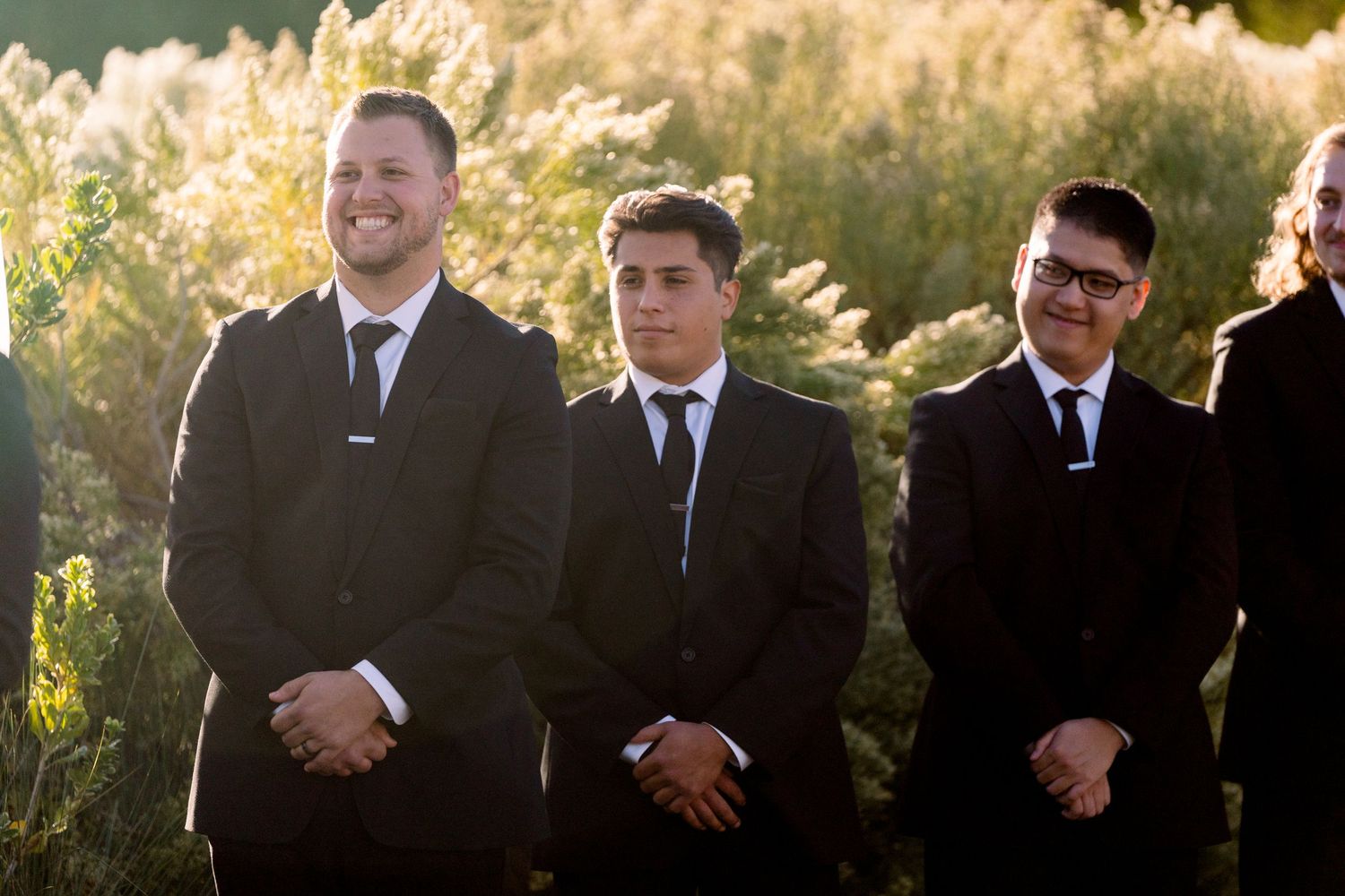 Groomsmen standing together during outdoor sunset ceremony.
