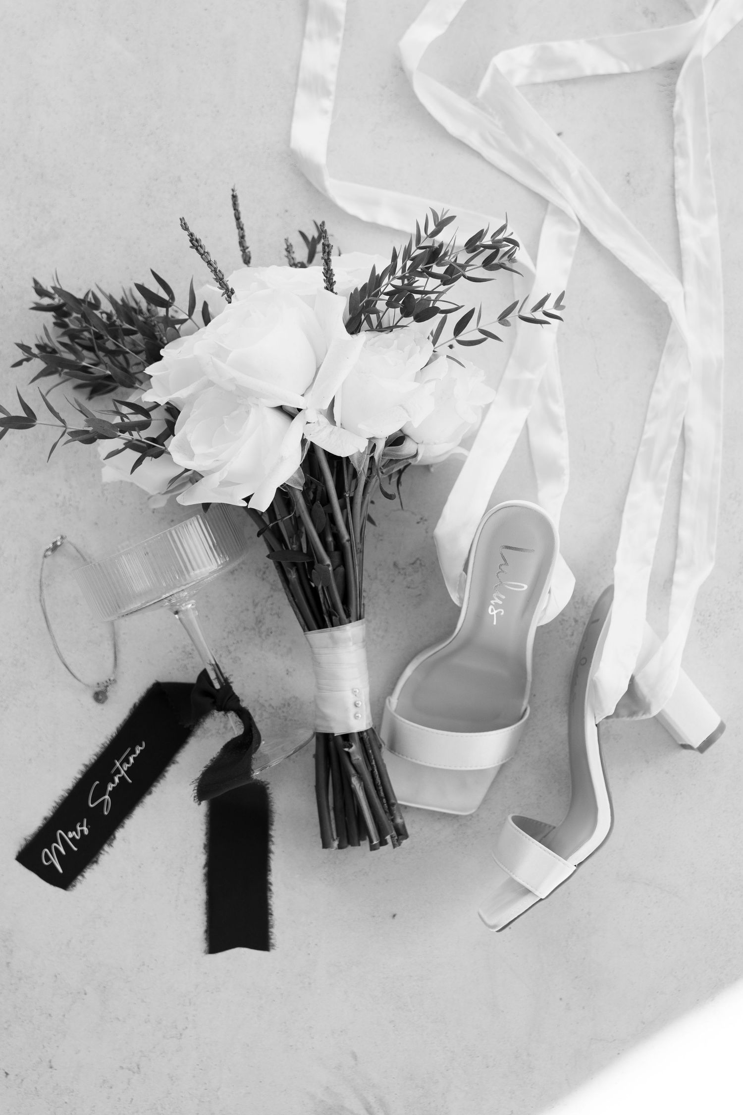 Wedding accessories including white floral bouquet and bridal shoes arranged on light surface.