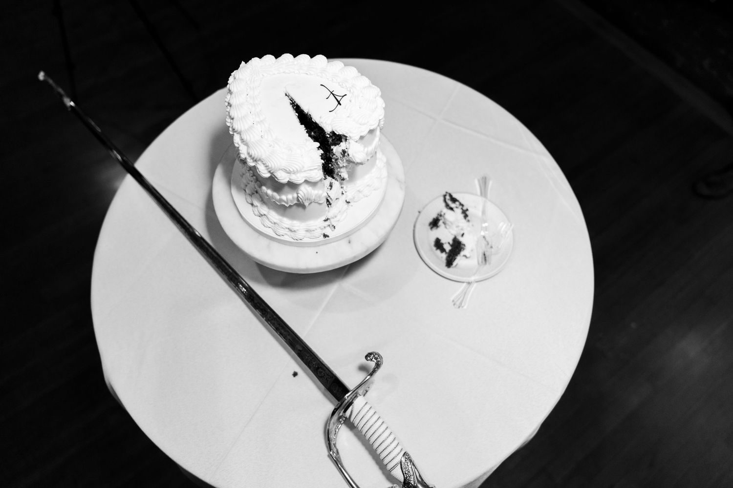 Black and white photo of a small white wedding cake and champagne glass on a round table.