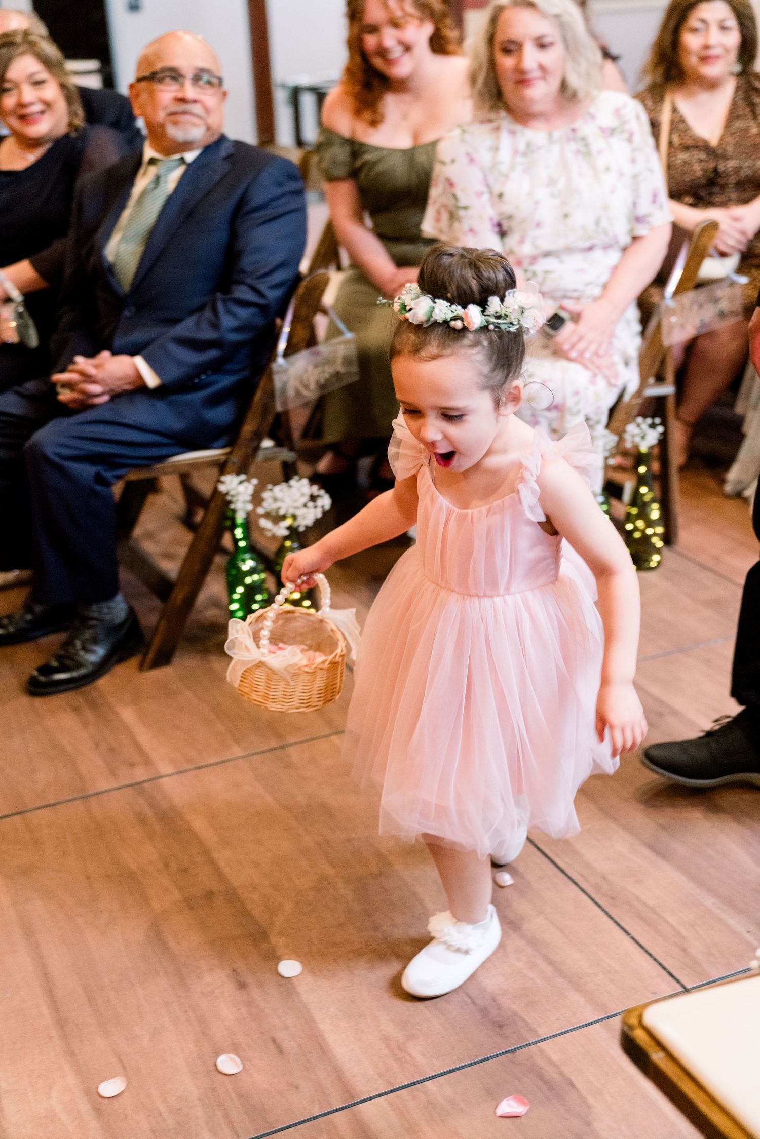 A young flower girl in a pink tulle dress dances joyfully on a wooden dance floor during a wedding celebration.
