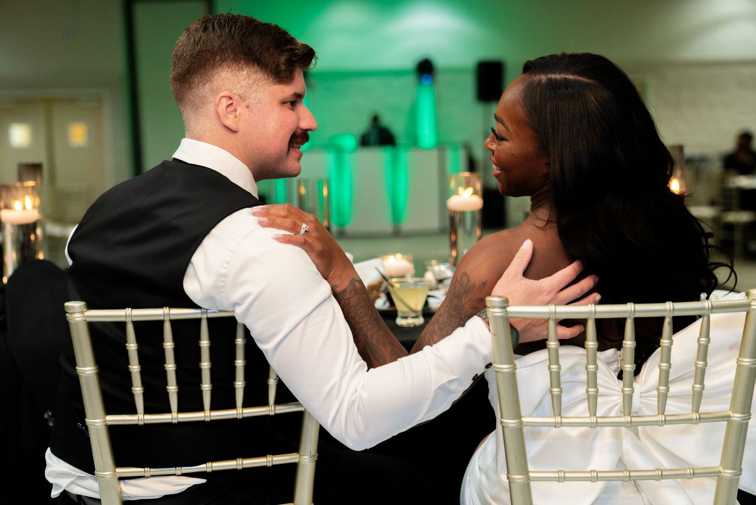 Wedding couple shares intimate moment while sitting at reception in chairs with green lighting.
