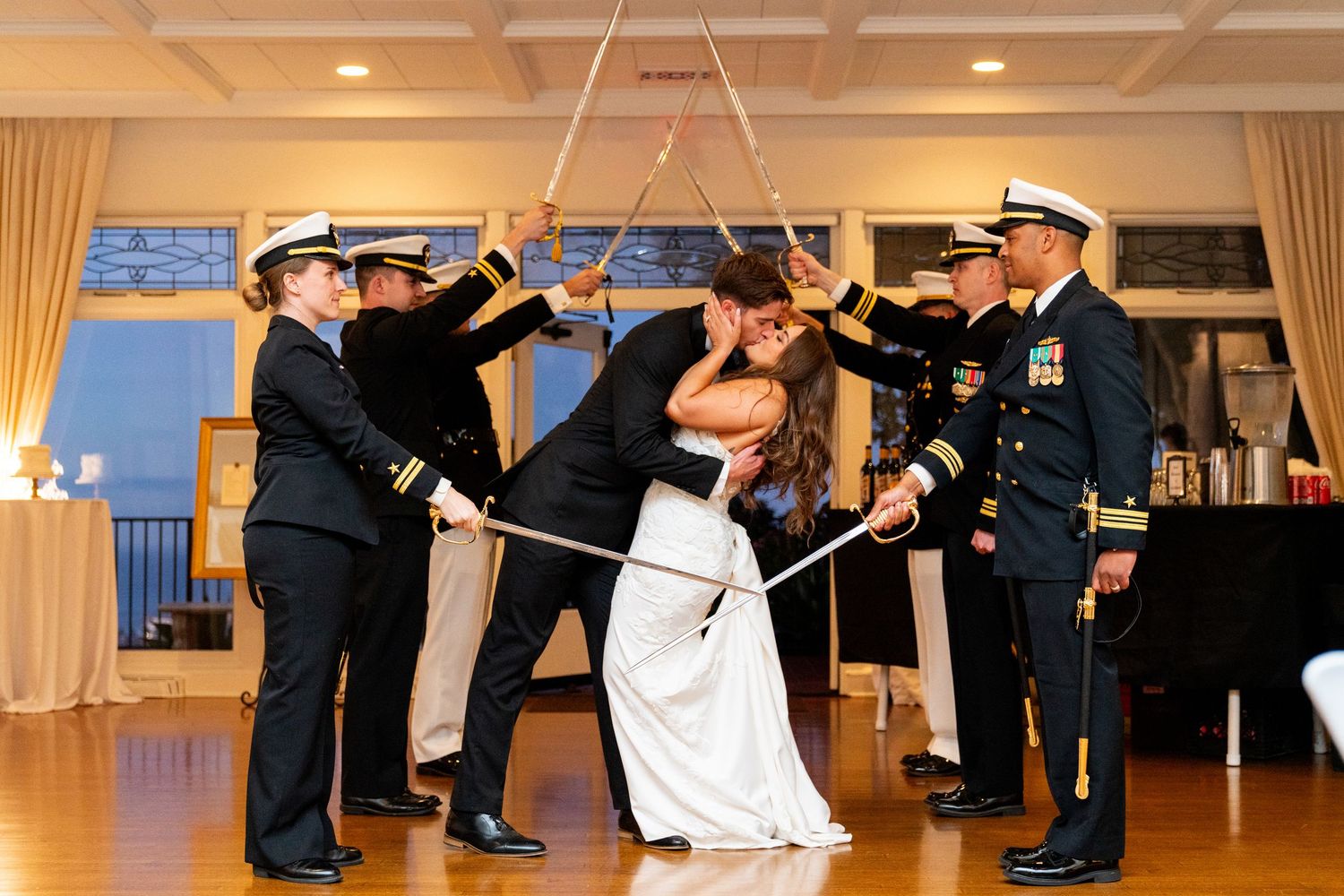 Military officers form a traditional sword arch for a couple during an indoor wedding ceremony.