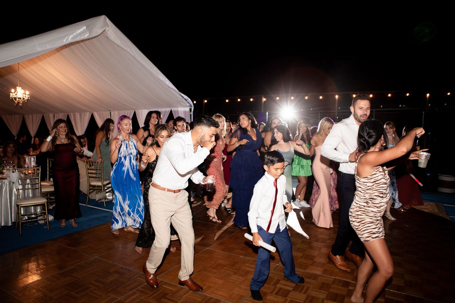 Wedding reception dance floor filled with guests enjoying lively celebration under tent.