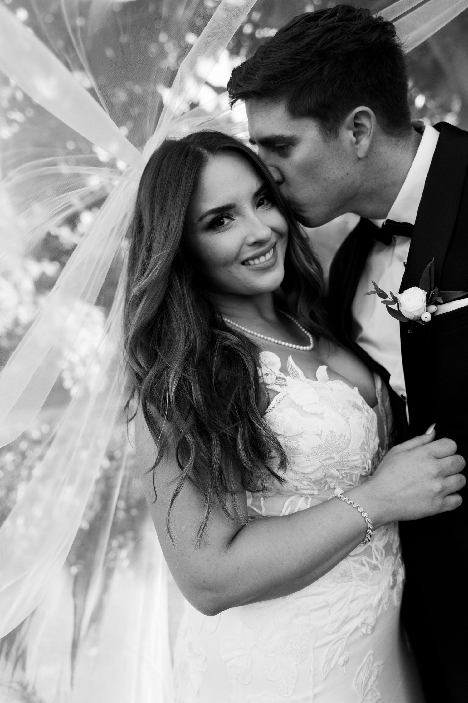 An intimate black and white wedding portrait showing tender moments under a flowing veil.