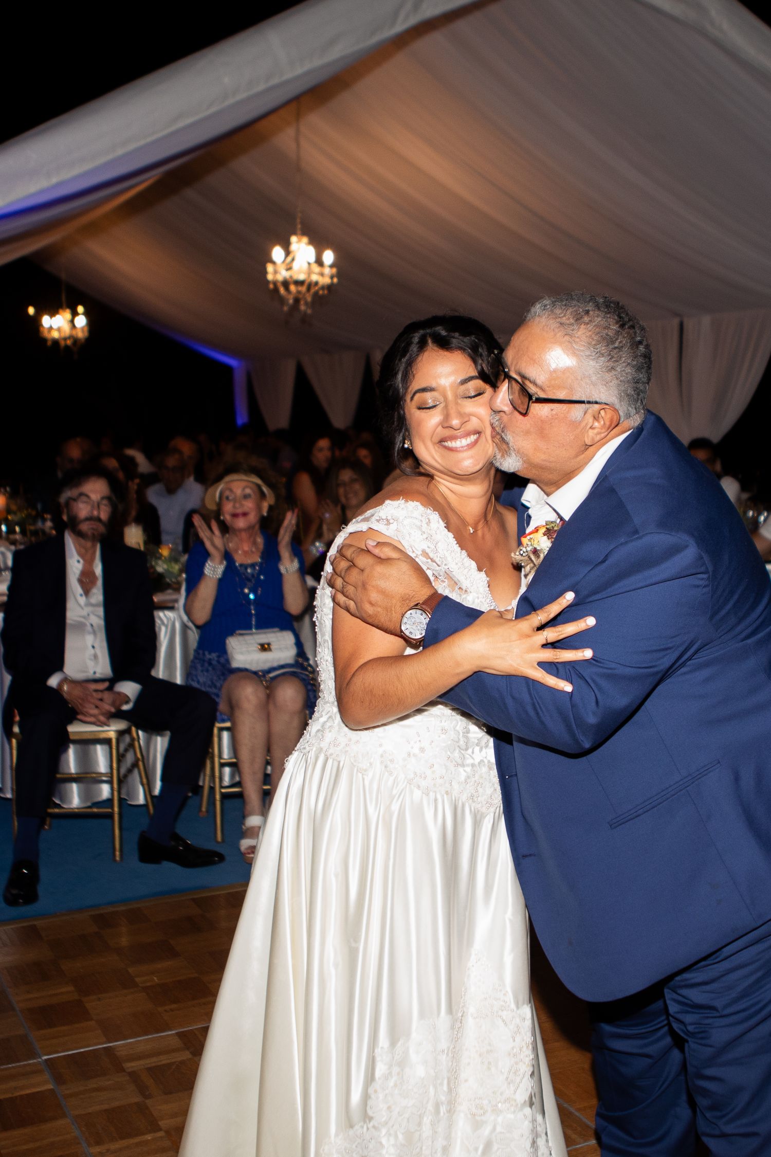 A joyful dance moment at an elegant tented wedding reception with chandeliers overhead.
