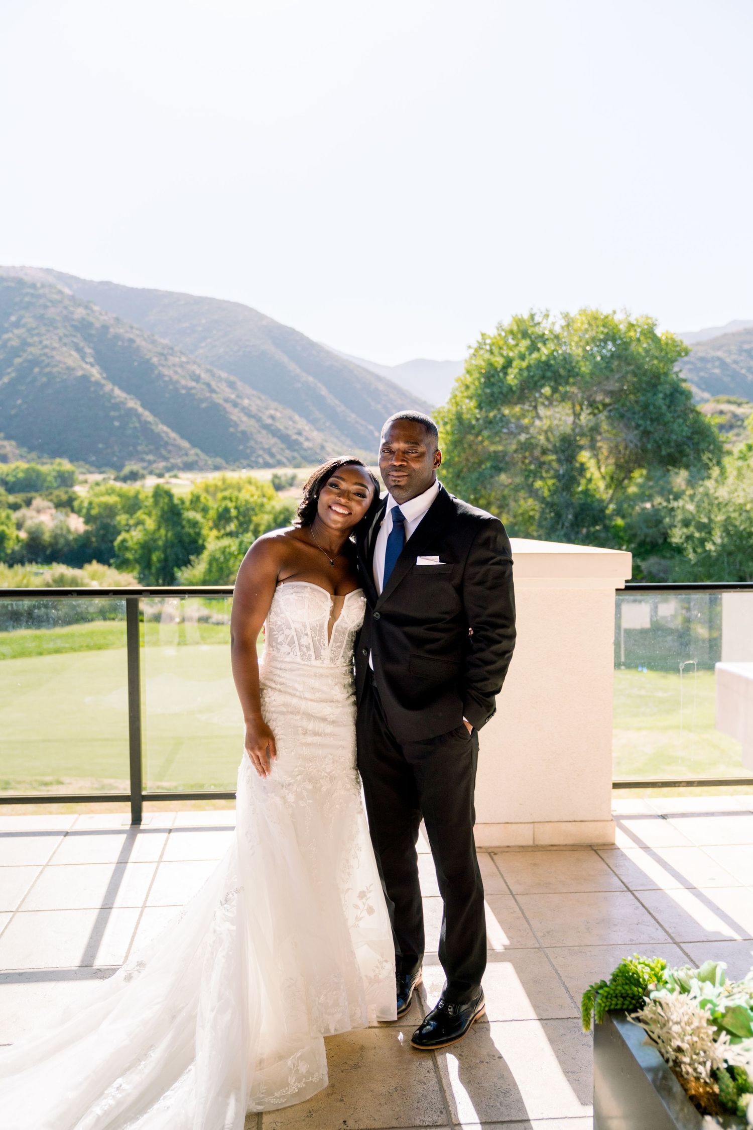 A wedding couple embraces on a terrace with scenic mountain views in the background.
