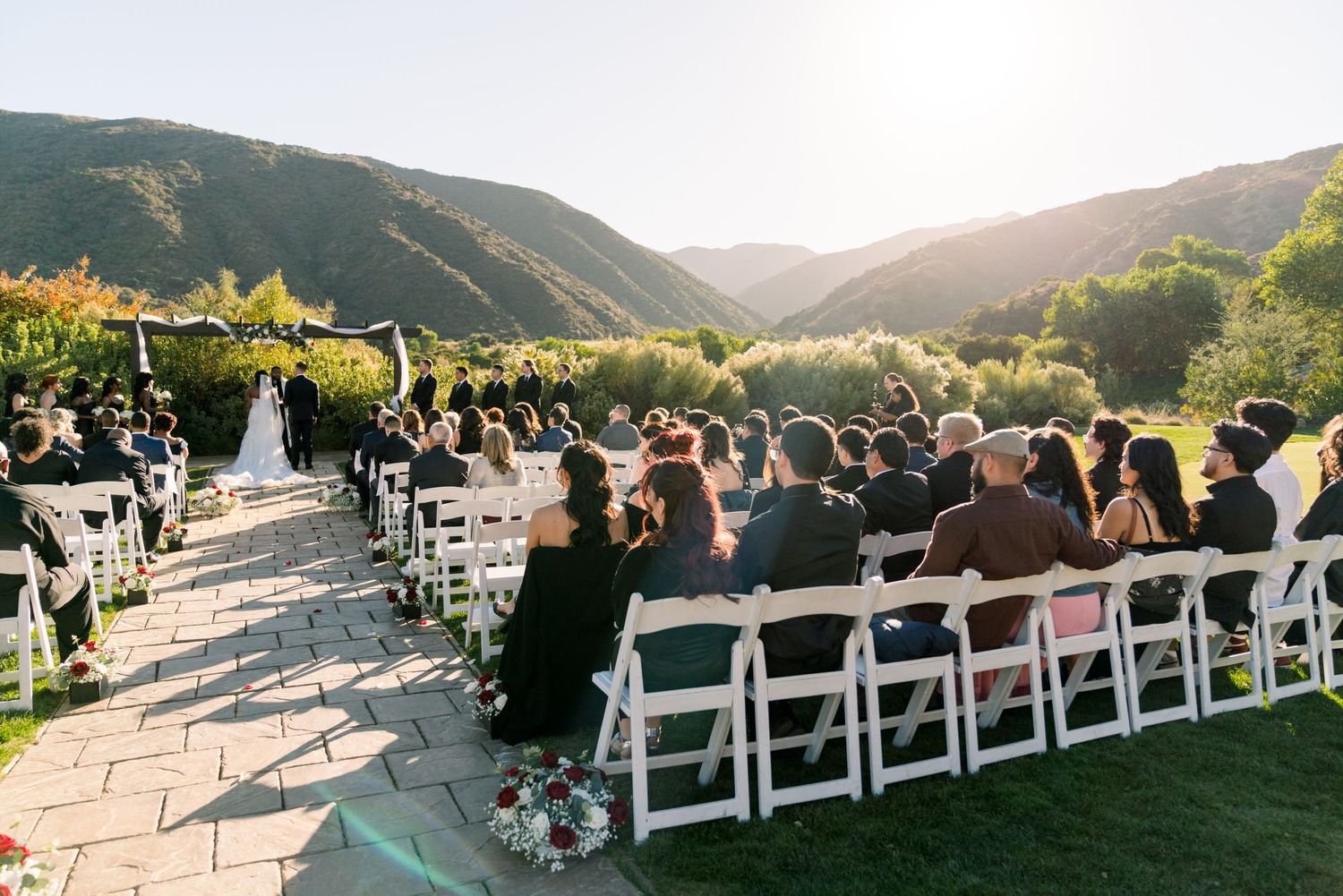 A scenic outdoor wedding ceremony setup with white chairs and mountain views at sunset.