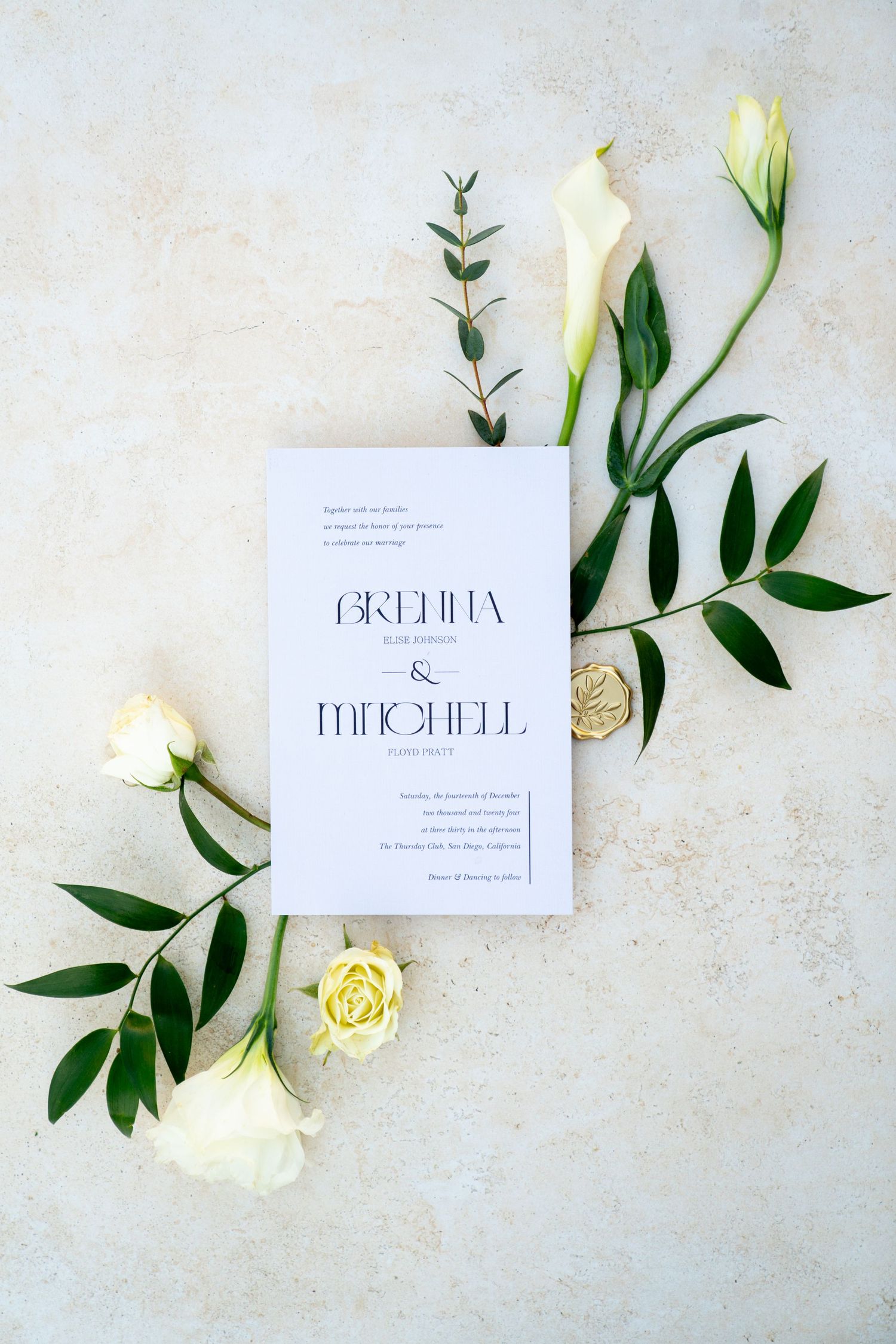 Wedding invitation with white roses and green foliage on a light textured background.