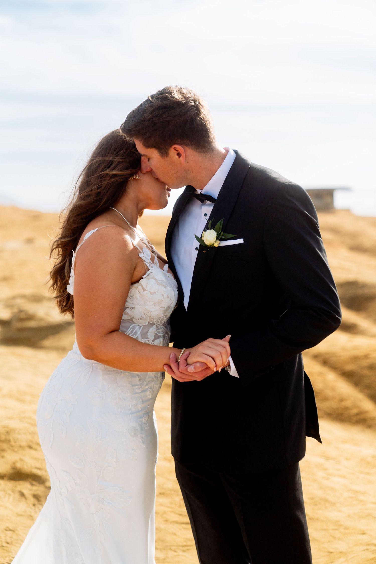 A tender wedding photo of newlyweds sharing an intimate moment against a golden hillside backdrop.