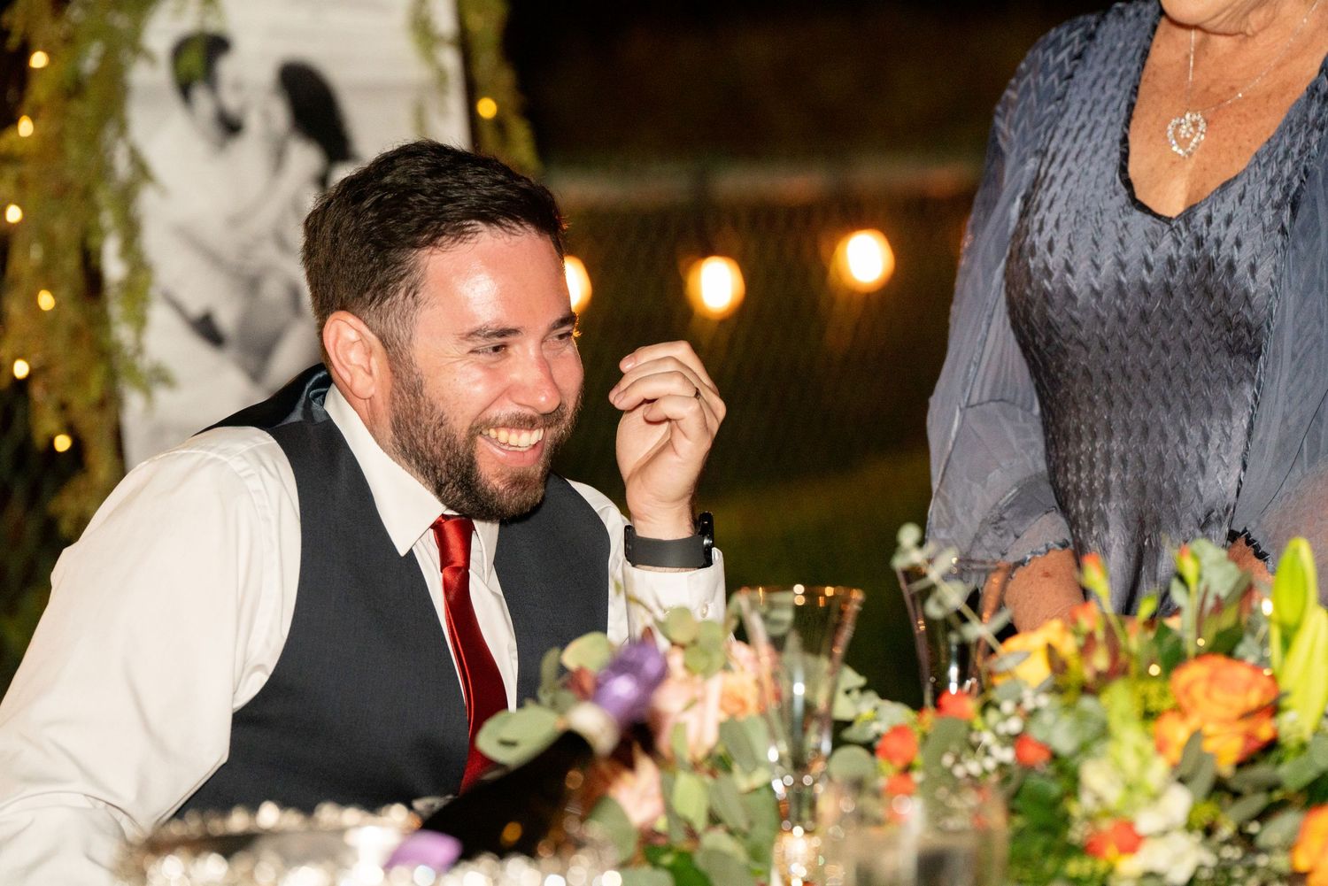 A joyful wedding guest enjoying dinner at an elegantly decorated outdoor reception under string lights.