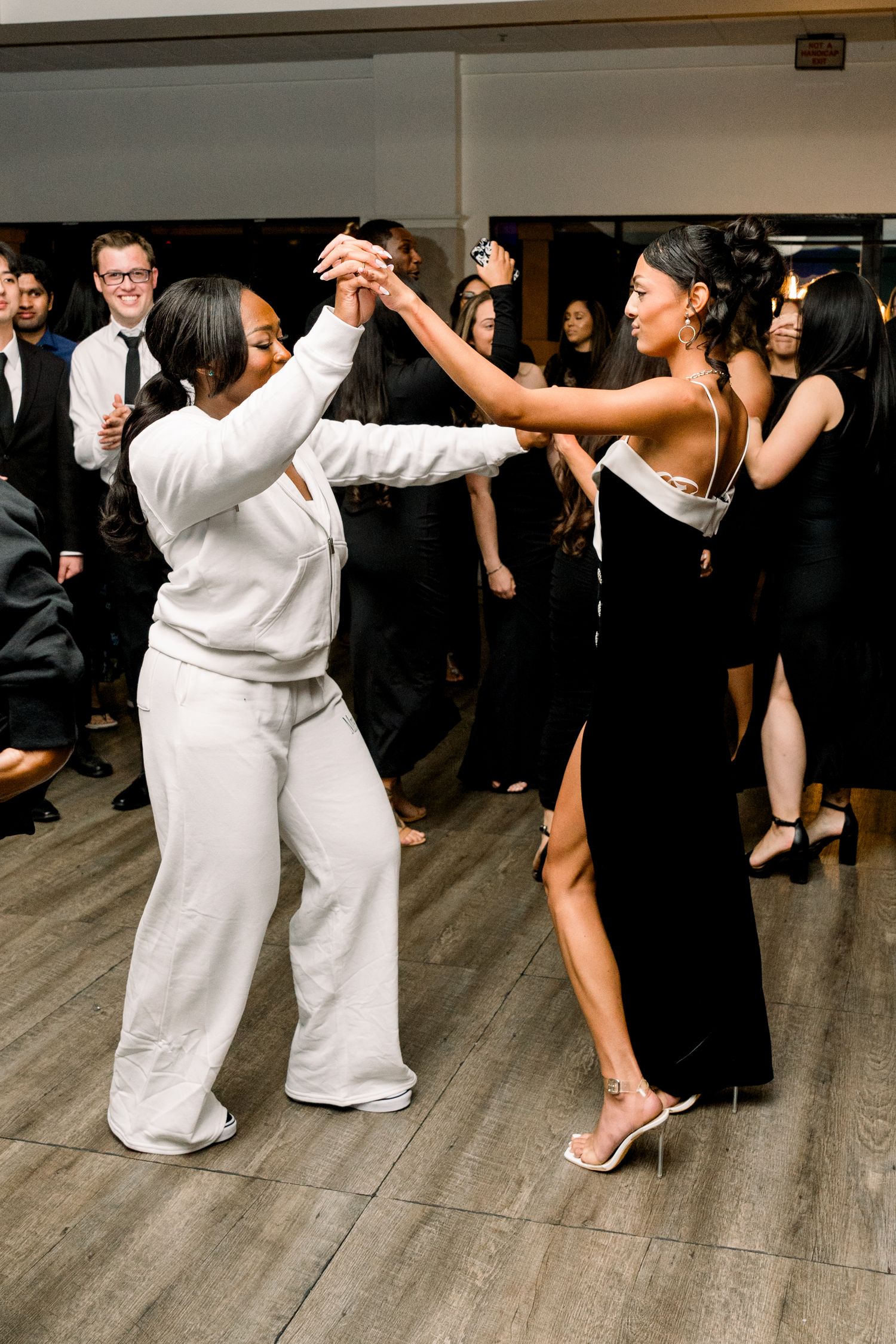 Wedding guests dancing together on a wooden dance floor during a reception celebration.