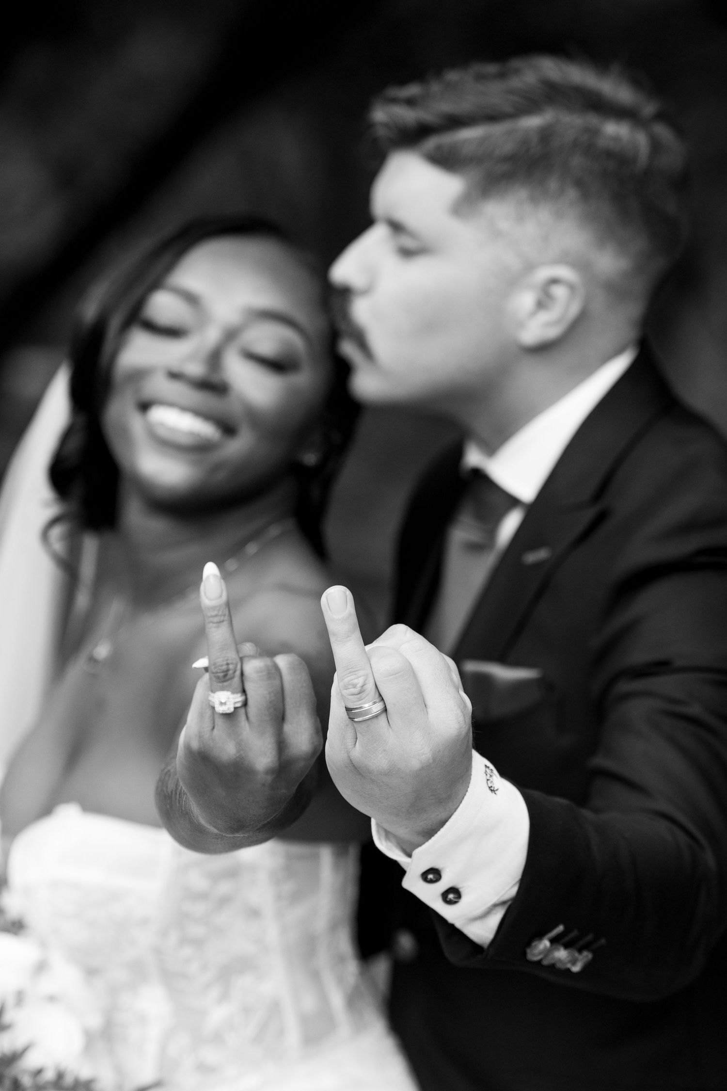 A newlywed couple shows off their wedding rings in a playful black and white photo.