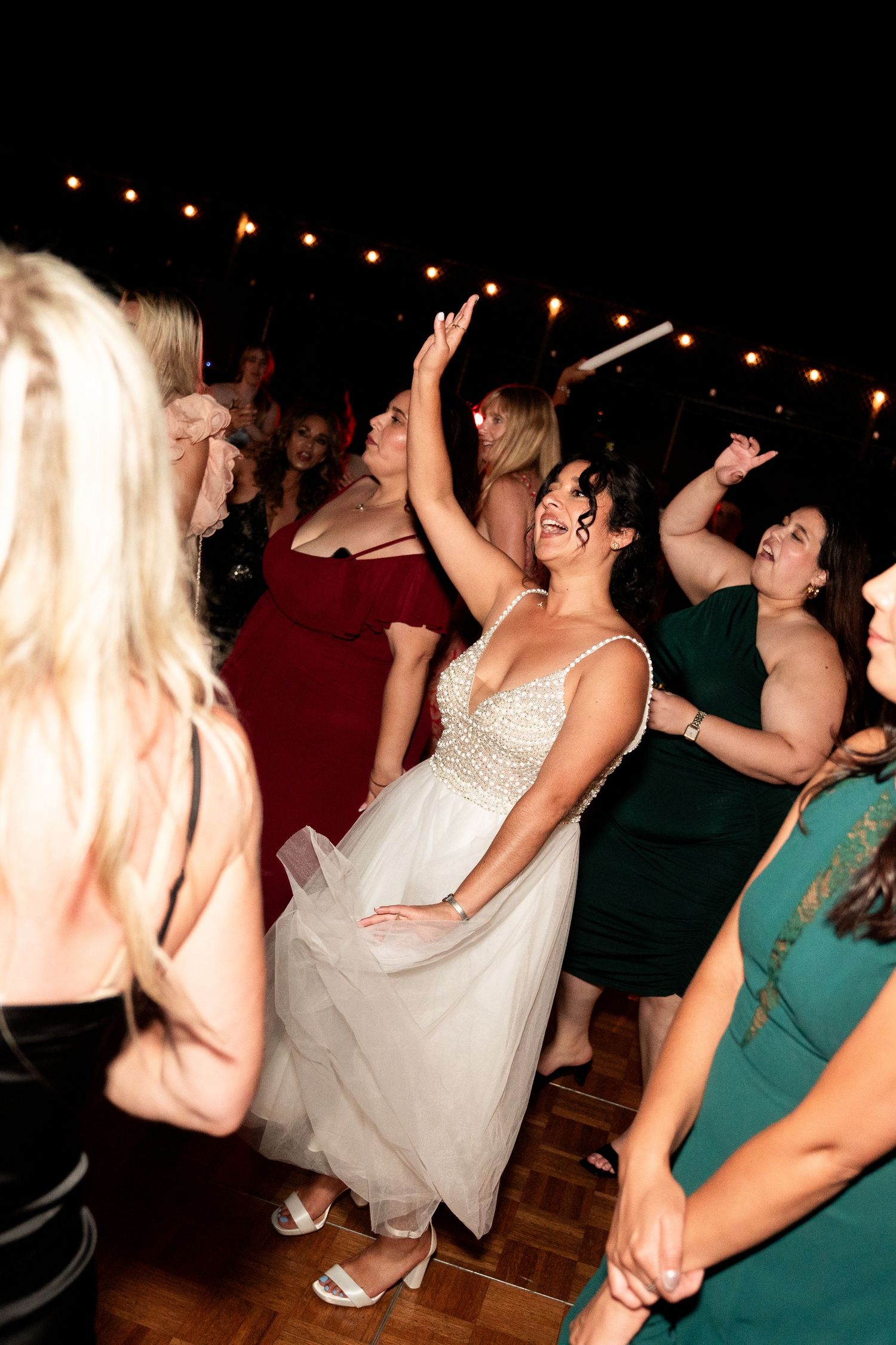 Wedding guests dancing together under string lights at nighttime celebration.