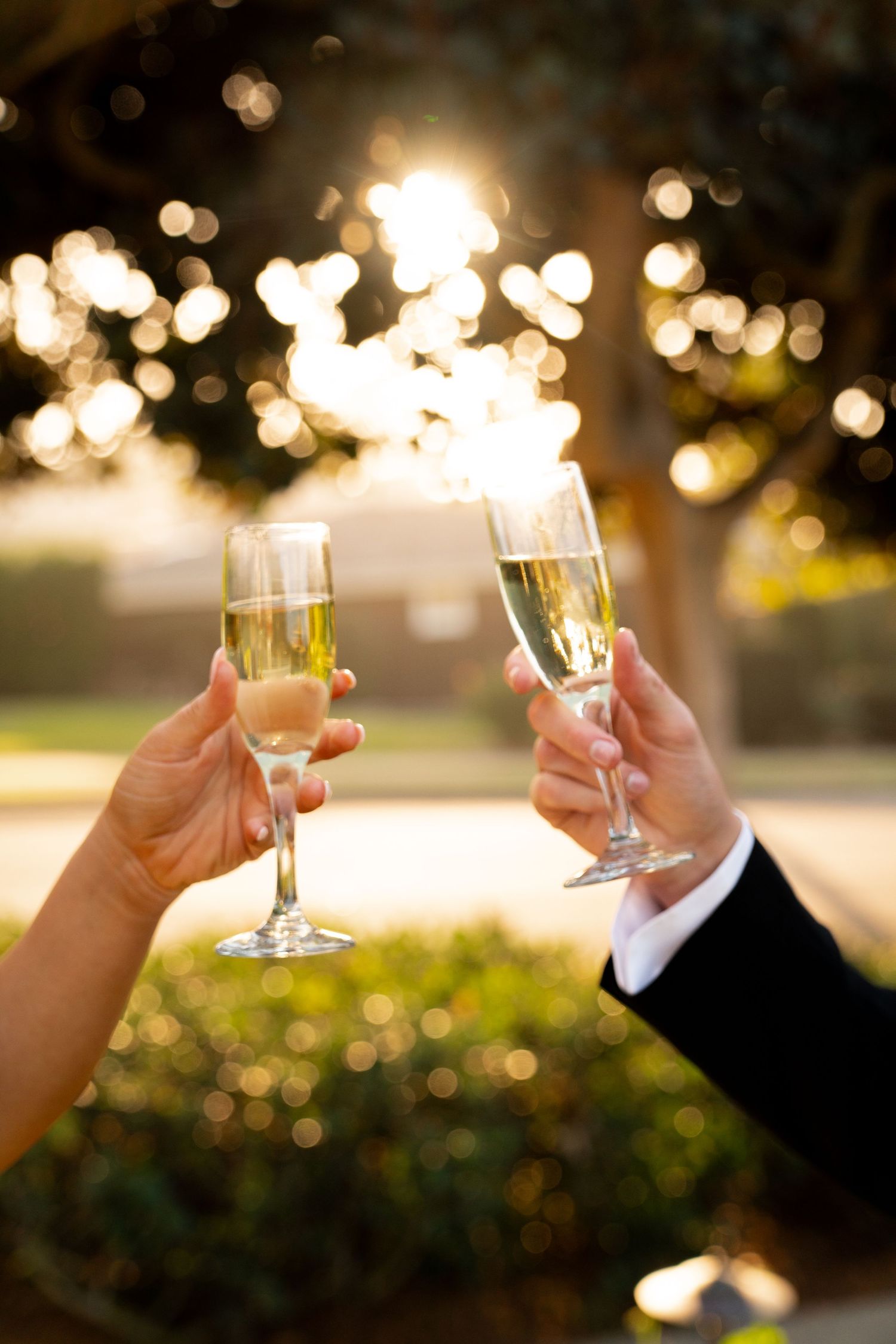 Two hands toasting with champagne flutes against a sunset bokeh background during a celebration moment.