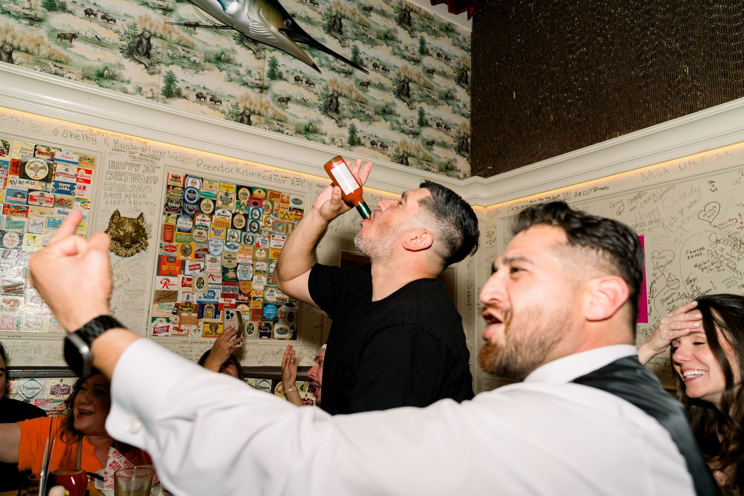 People having fun at a party scene with drinks and animated expressions in an indoor setting.