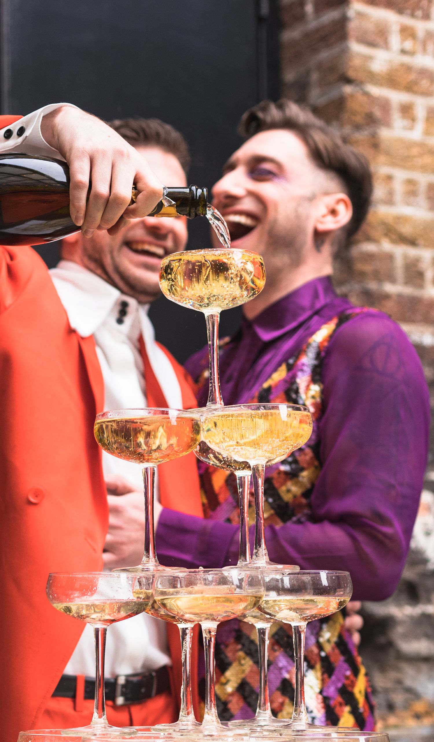 Couple pouring champagne into champagne glass tower while laughing