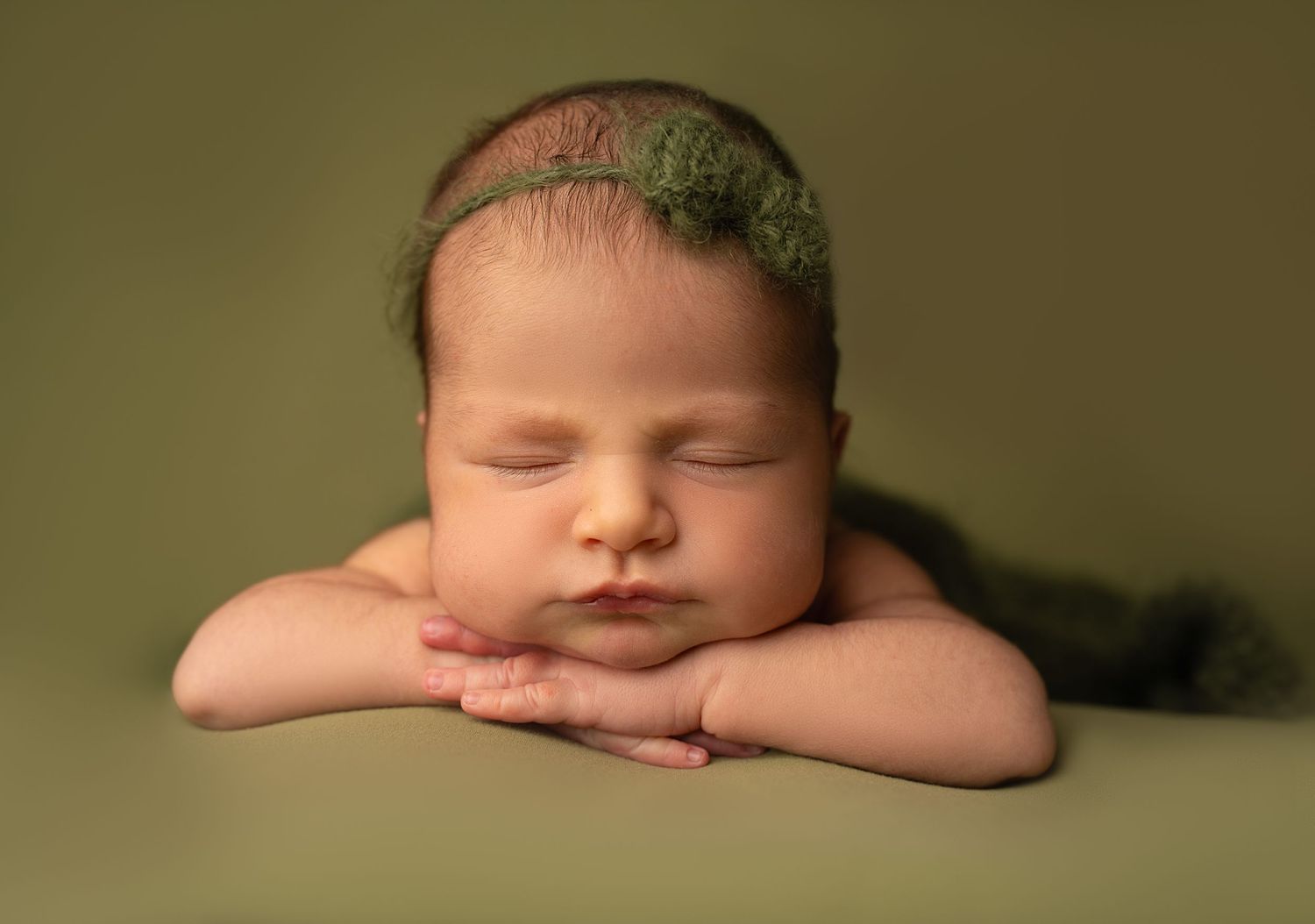 Serene newborn portrait on olive green backdrop with simple natural styling.