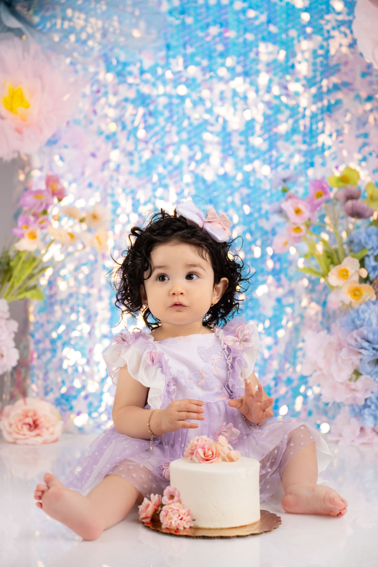 Cake smash photoshoot with sparkly blue backdrop and floral decorations.