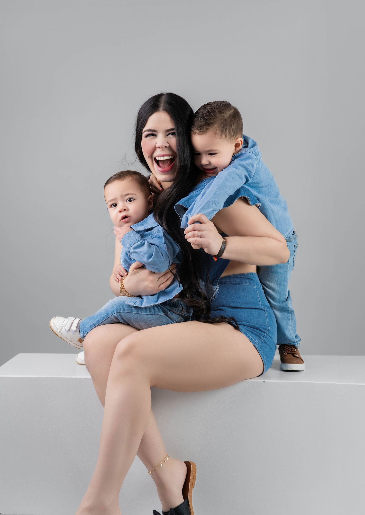 A joyful family wearing coordinating denim outfits poses together against a gray background.