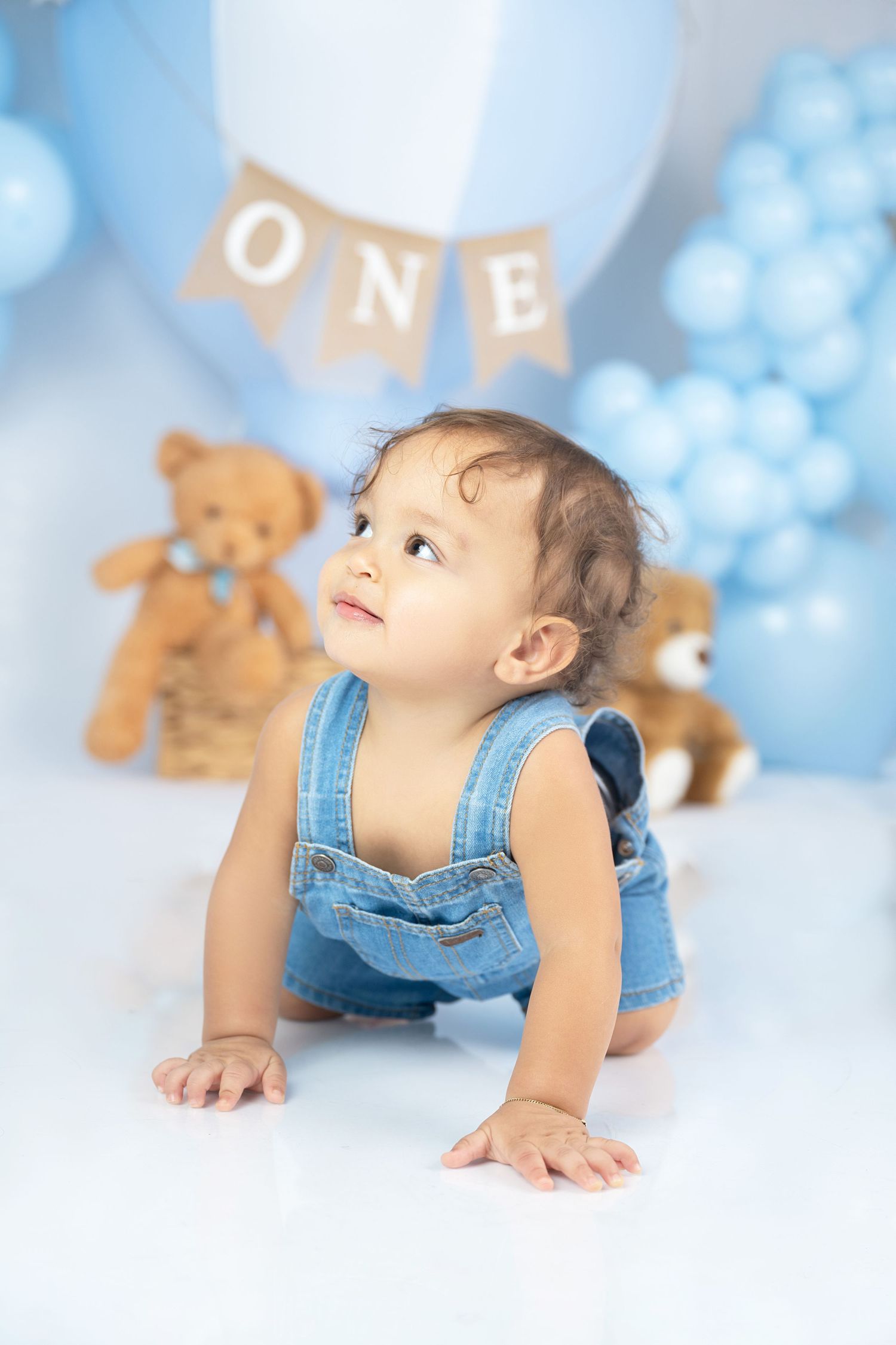 A first birthday setup with denim overalls, teddy bears, and blue balloons in the background.