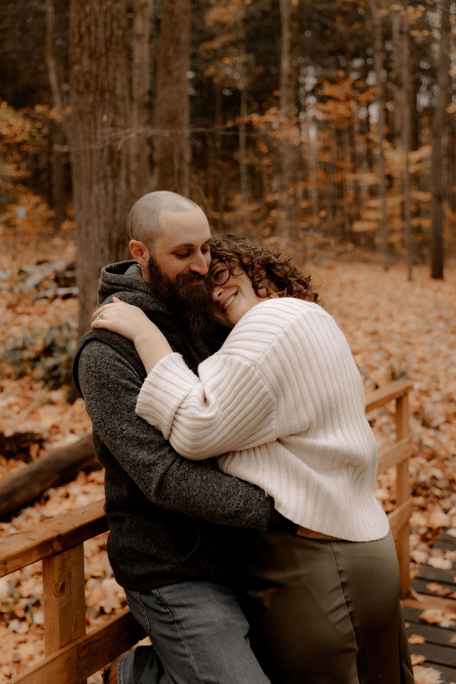 Intimate embrace on a wooden walkway surrounded by autumn trees.
