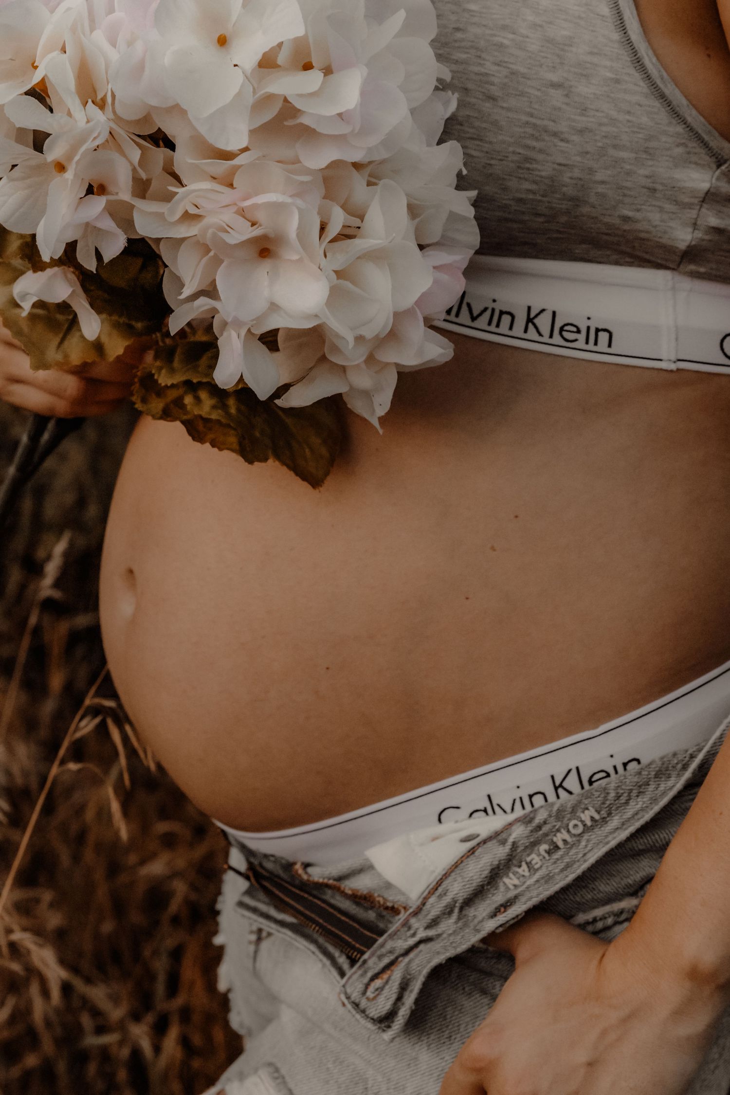White floral bouquet held near Calvin Klein underwear waistband in warm muted tones.