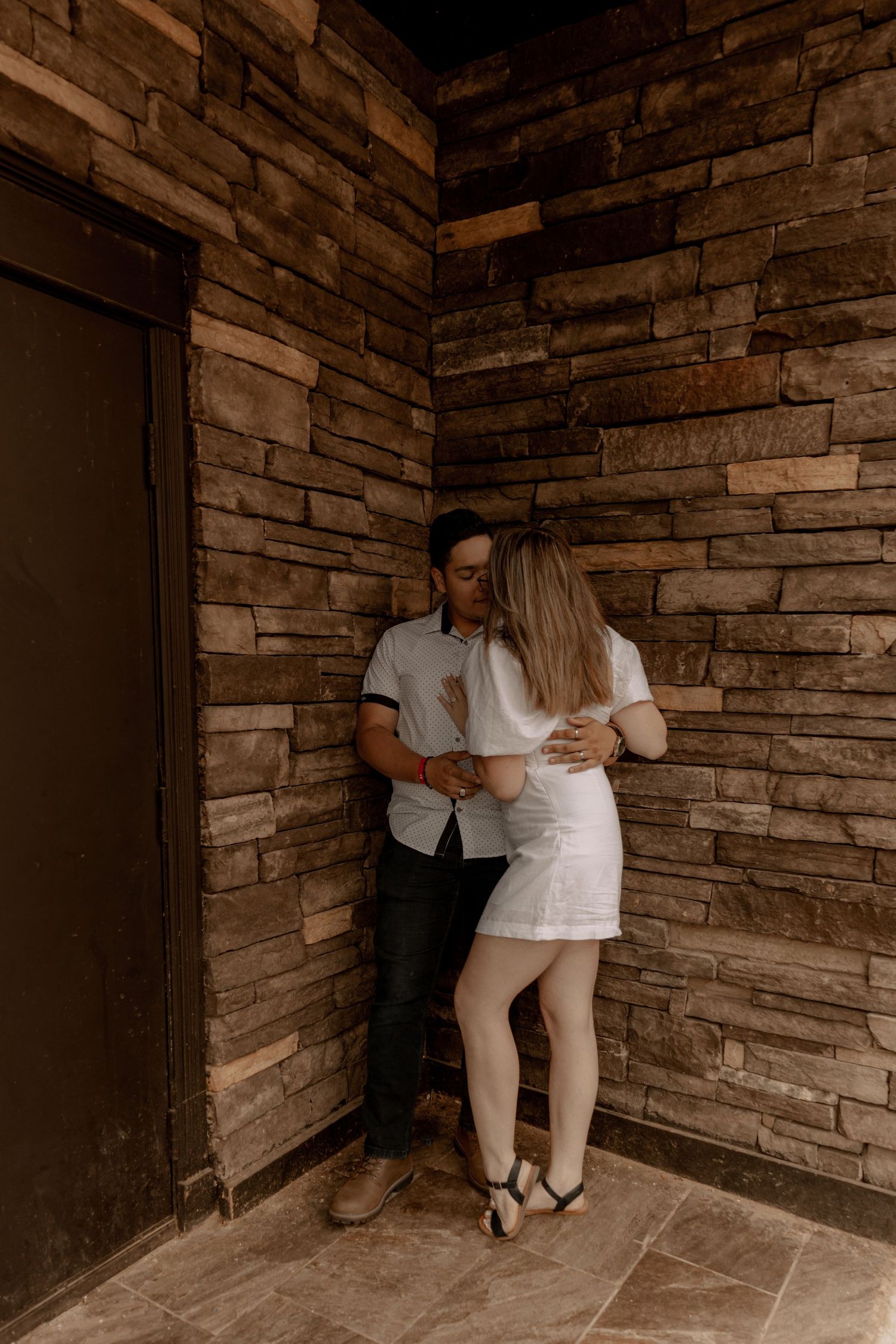 A couple shares an intimate moment in a corner of a stone-walled building with rustic architectural features.